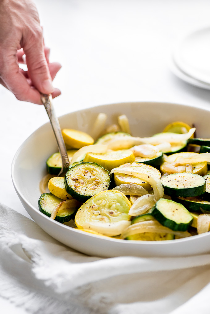 Sautéed Zucchini and Squash in a serving bowl with a hand lifting some out with a spoon.