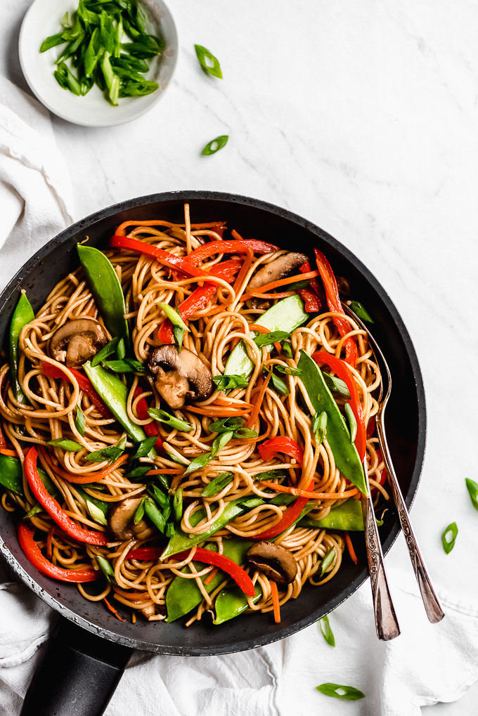 Lo Mein in a skillet with spoons on the side and a small dish of green onions off to the side.