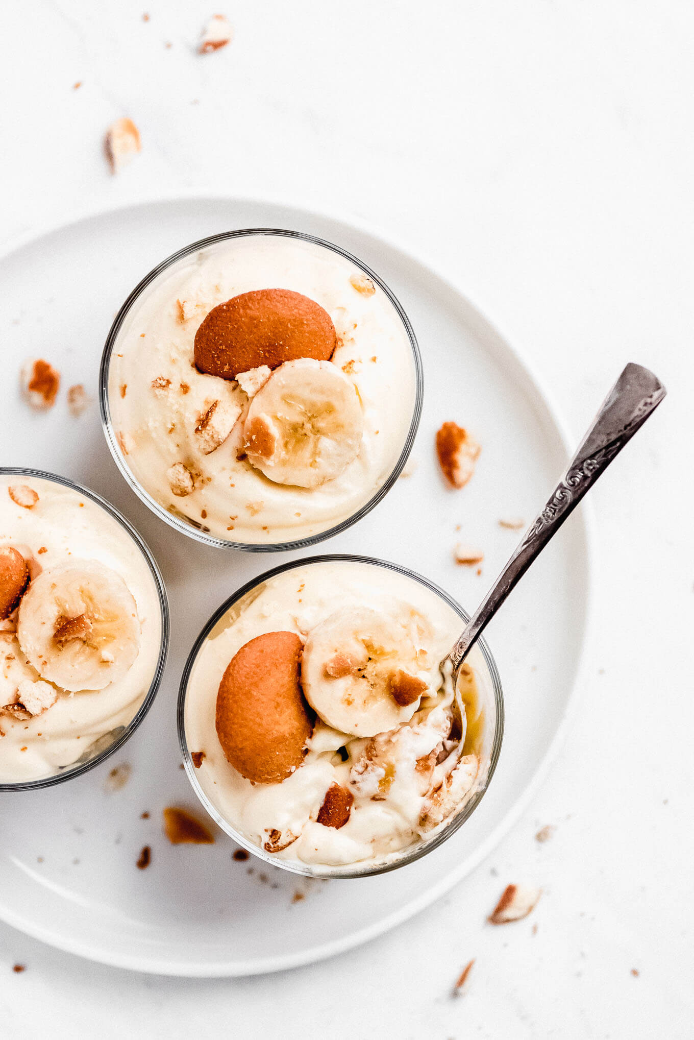A plate with 3 glass dishes of vanilla pudding topped with vanilla cookies and bananas.