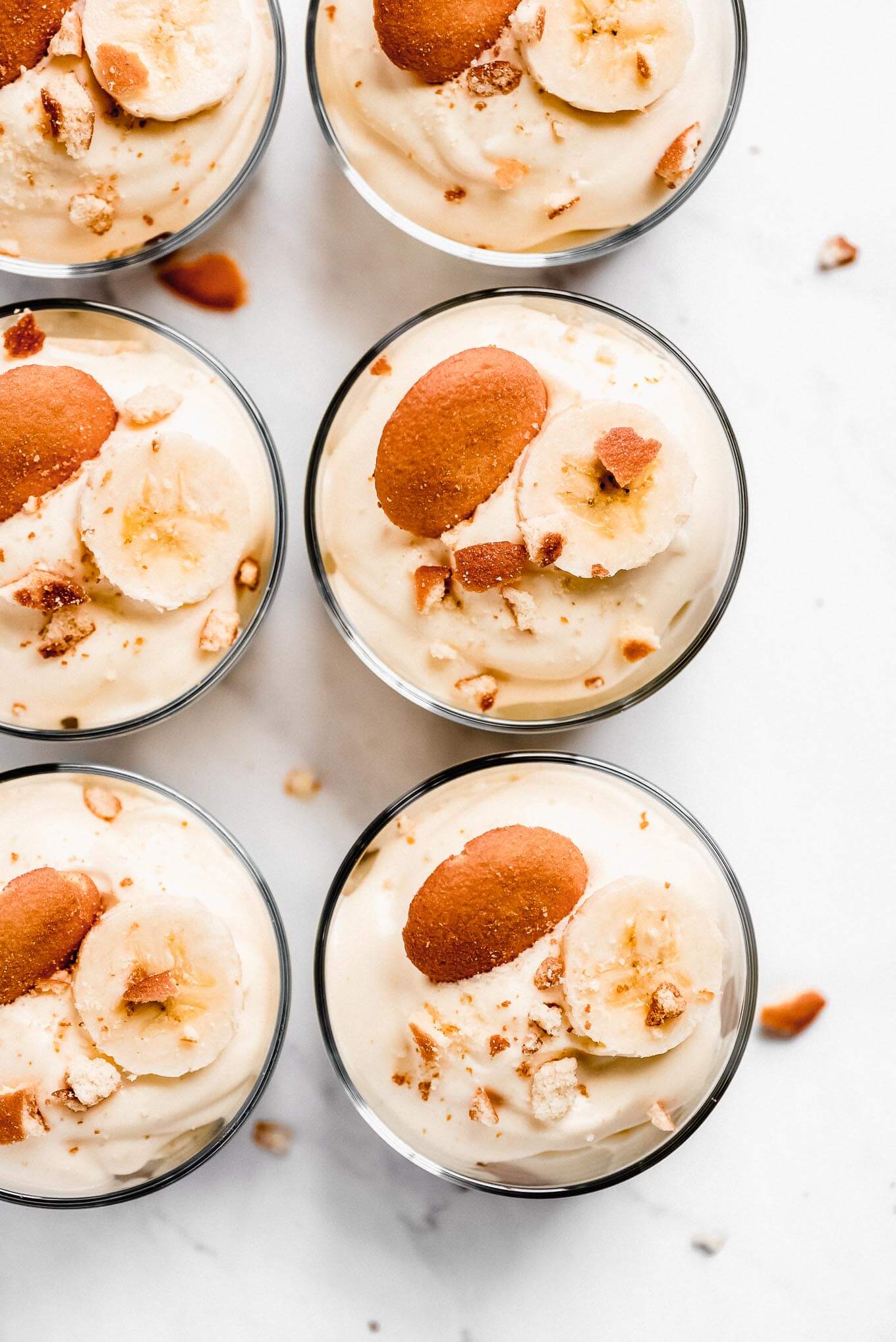 Top view of six jars of Banana Pudding with a Nilla Wafer, banana slice, and crushed Nilla Wafers.