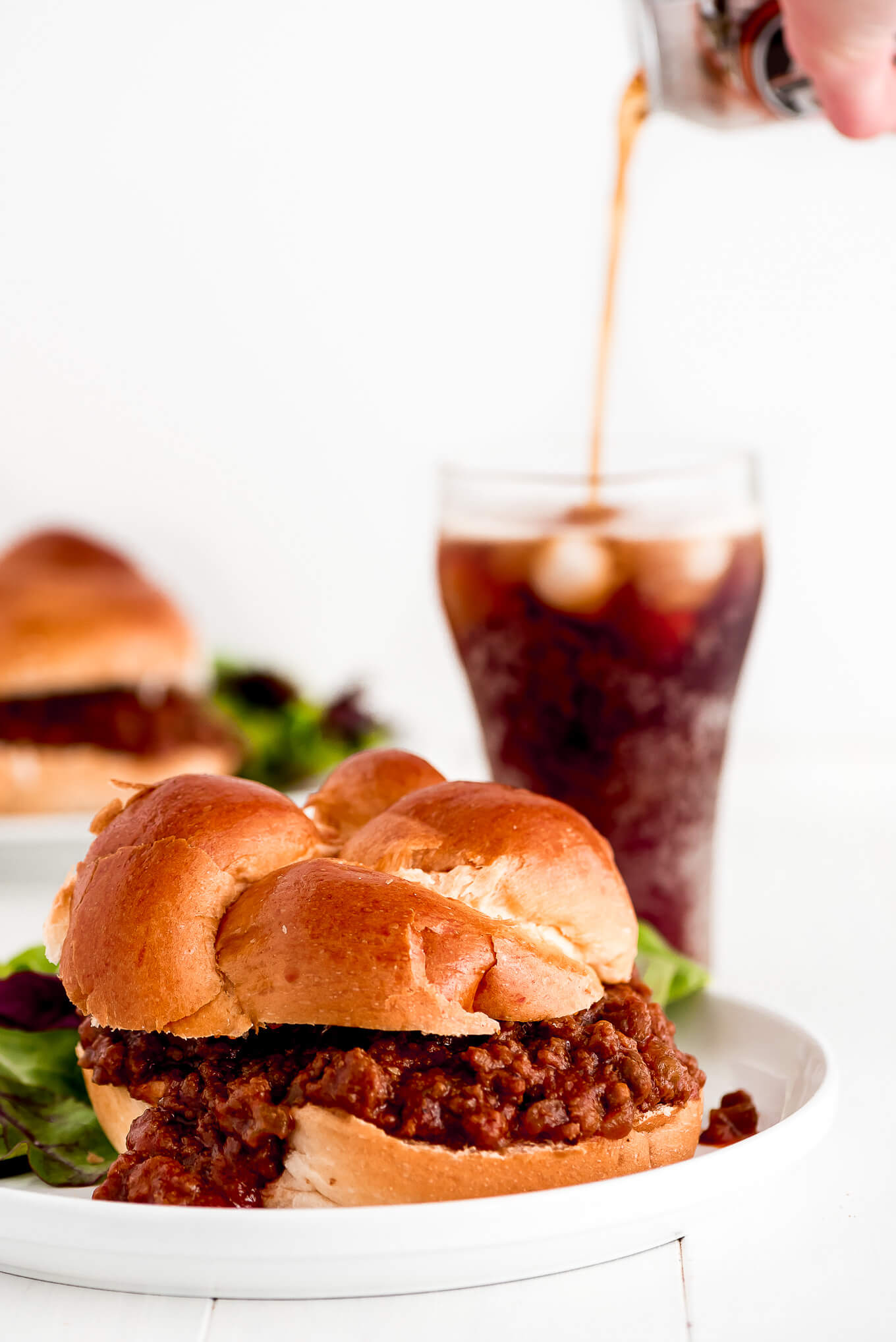 Sloppy Joes made with challah buns on plates with soda being poured into a glass in the background.
