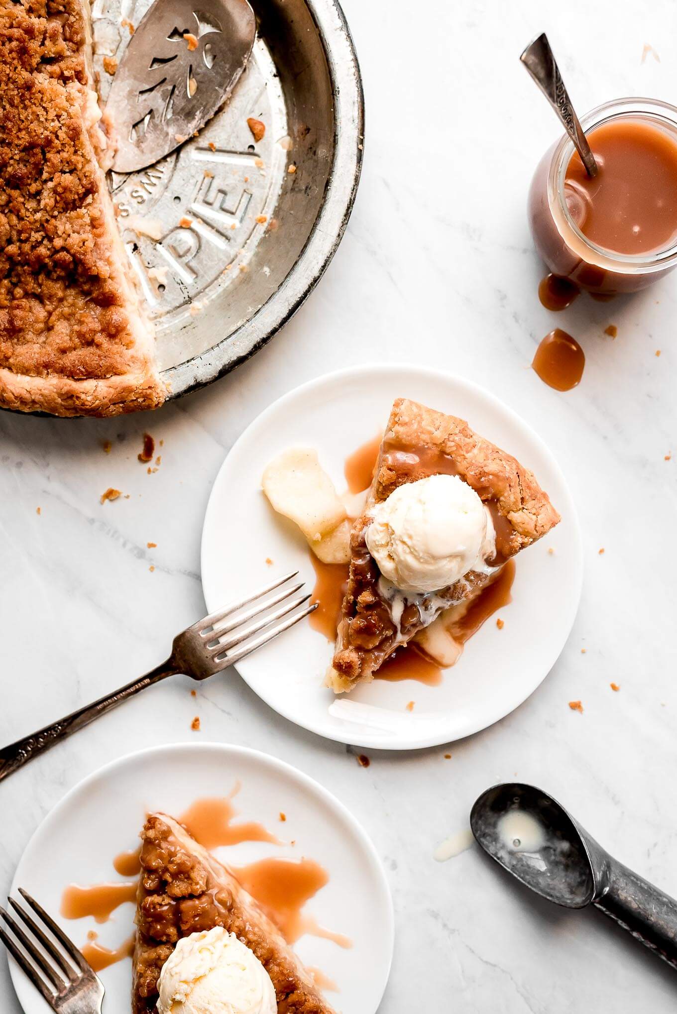 Slices of Dutch Apple Pie on plates topped with ice cream and caramel sauce.