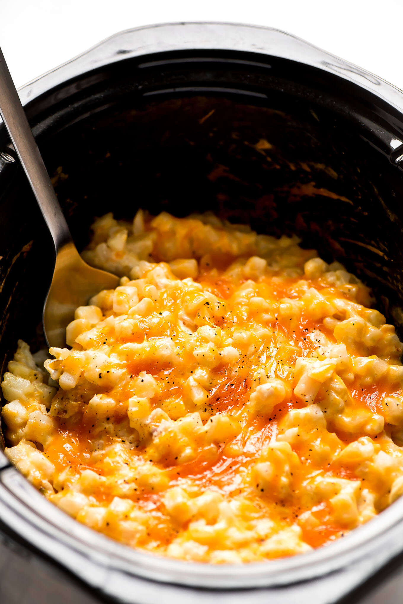 Slow Cooker Cheesy Potatoes in a Crock-Pot with a spoon lifting some out.