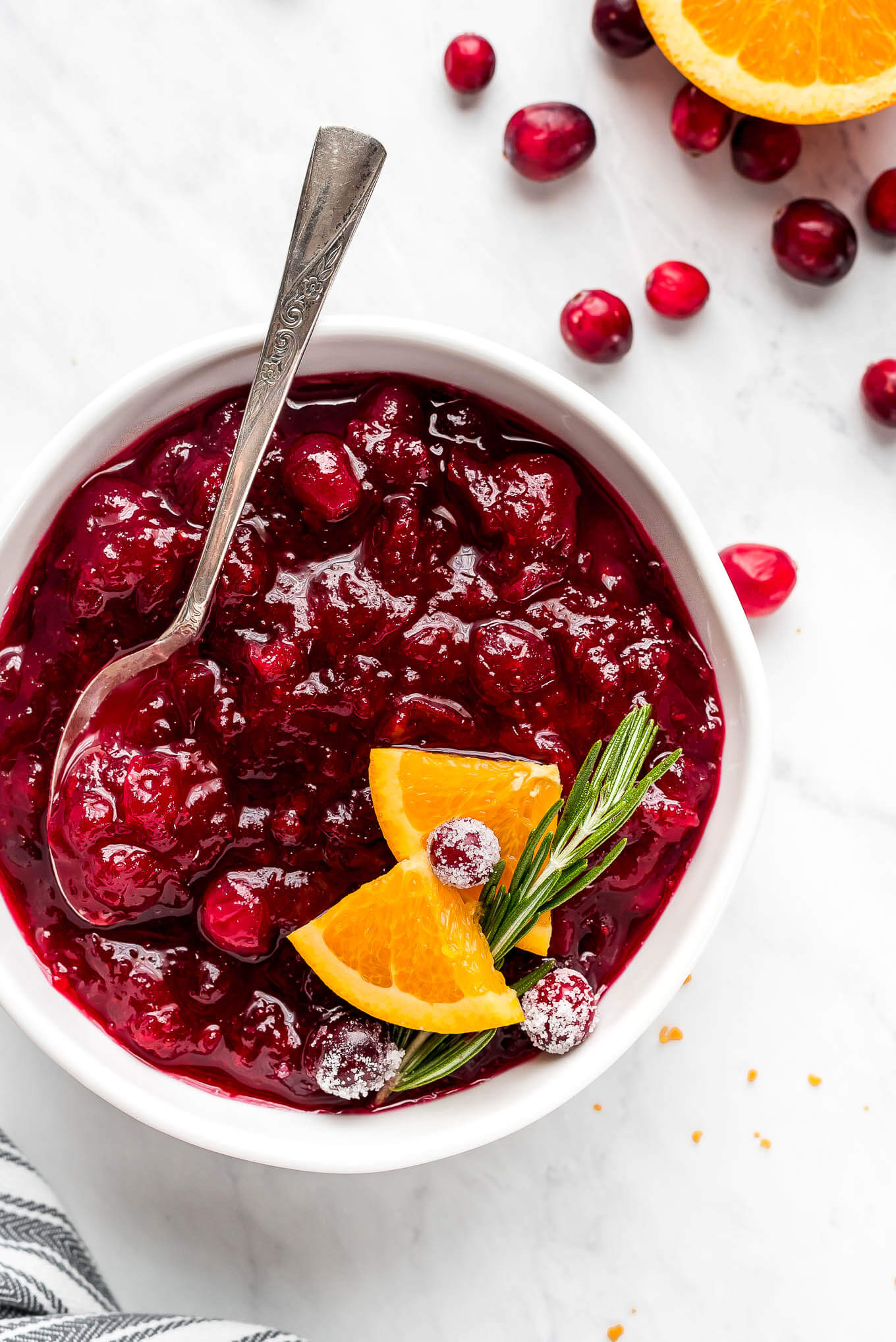 A bowl of Cranberry Sauce garnished with orange slices, rosemary, and sugared cranberries.