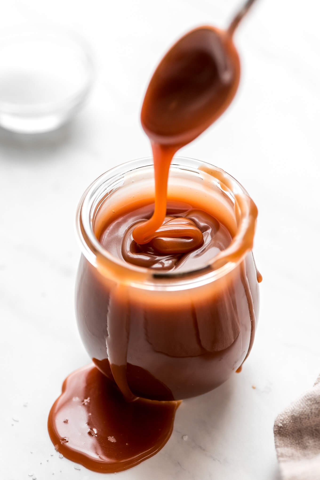 Caramel drizzling down from a spoon into a jar of salted caramel sauce.