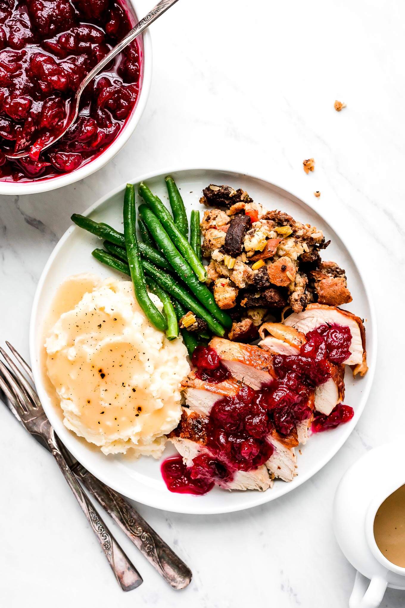 A plate of Thanksgiving dinner- herb butter tureky, cranberry sauce, mashed potatoes and gravy, green beans, and stuffing.