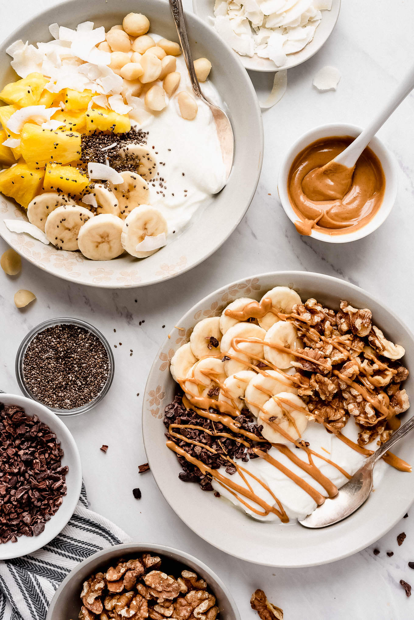 A yogurt bowl with tropical toppings and a yogurt bowl with nuts, bananas, and chocolate.