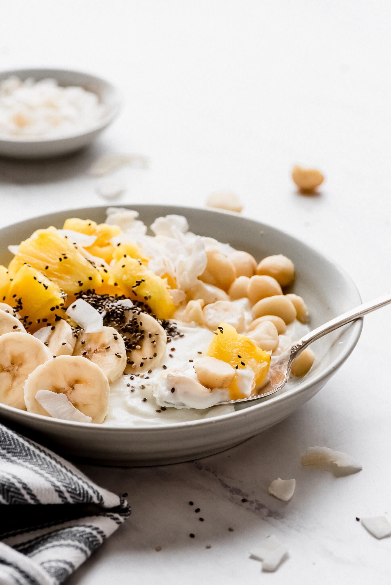 A Greek yogurt bowl topped with bananas, pineapple, chia seeds, coconut flakes, and macadamia nuts.