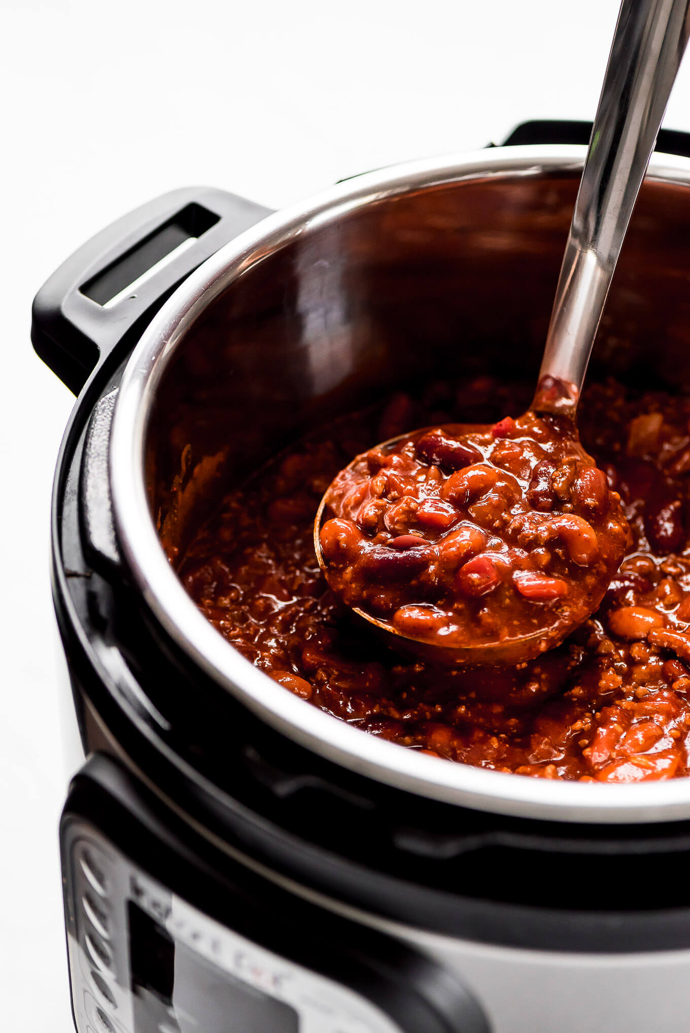 A ladle full of chili being lifted out of a pressure cooker.