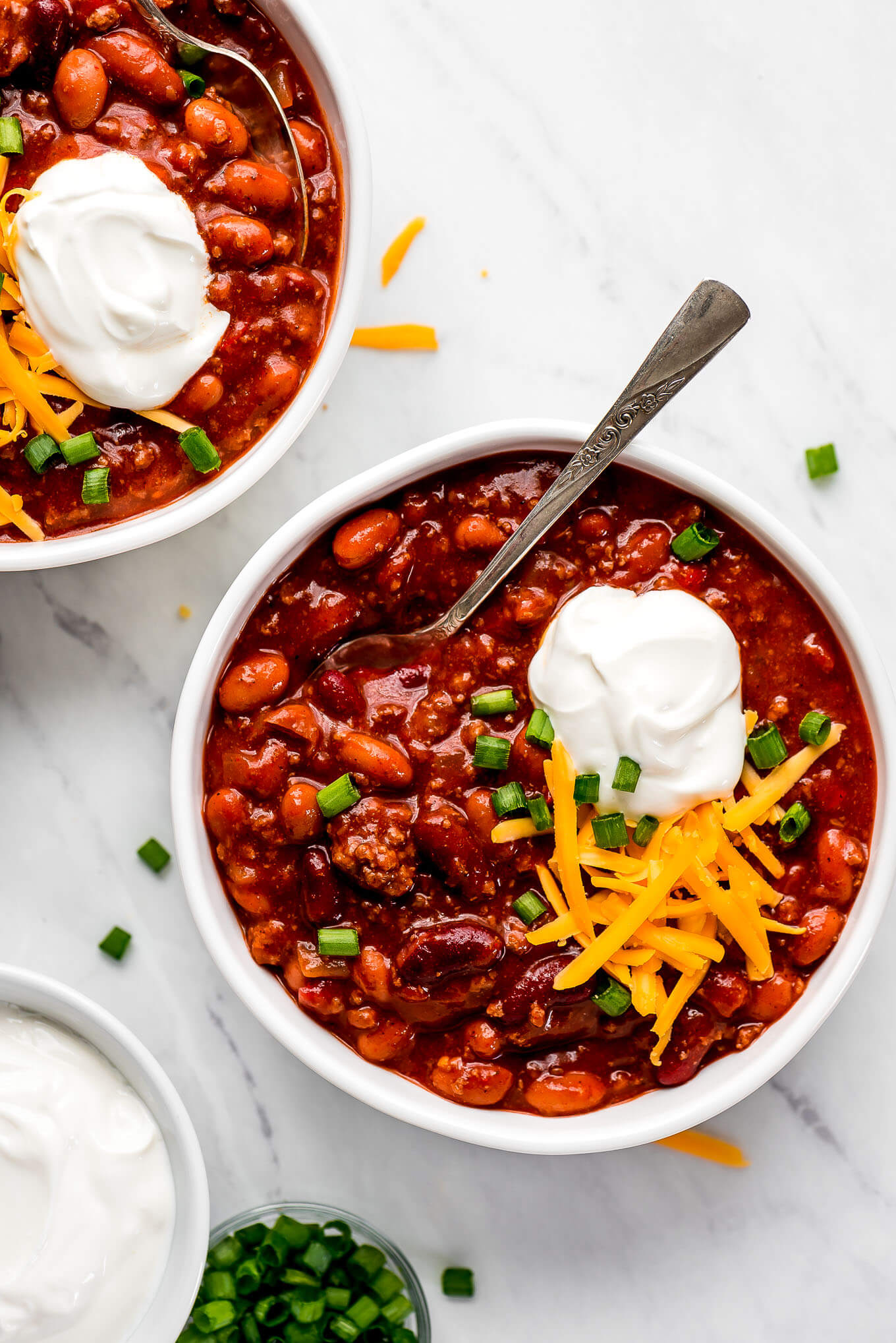 Two bowls of Instant Pot Chili with toppings and spoons in them.