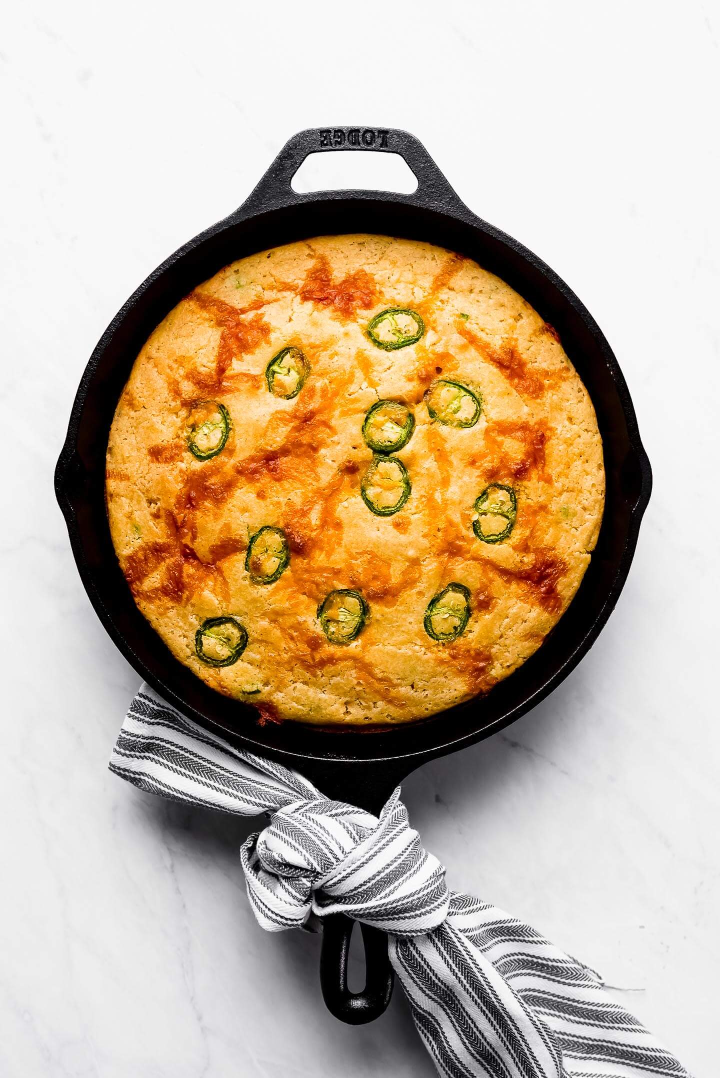Jalapeno Cheddar Skillet Cornbread in a cast iron skillet with a towel tied around the handle.