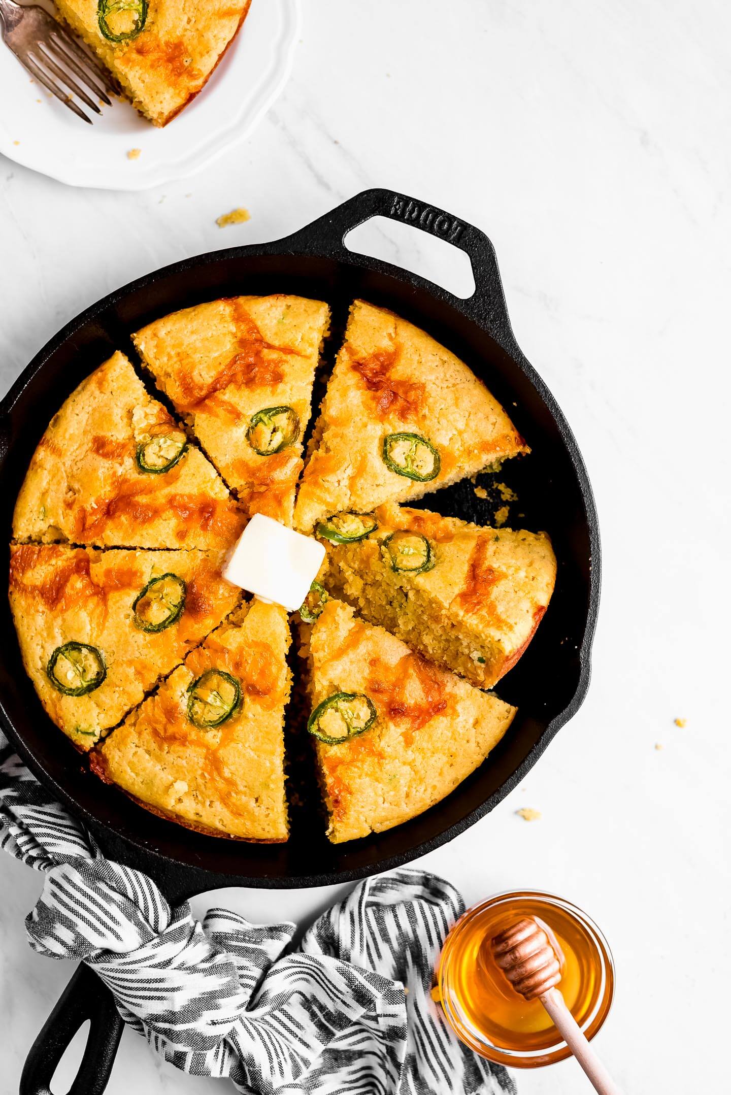 Jalapeno Cheddar Cornbread cut into triangle shape slices in a cast iron skillet and a pat of butter on top.