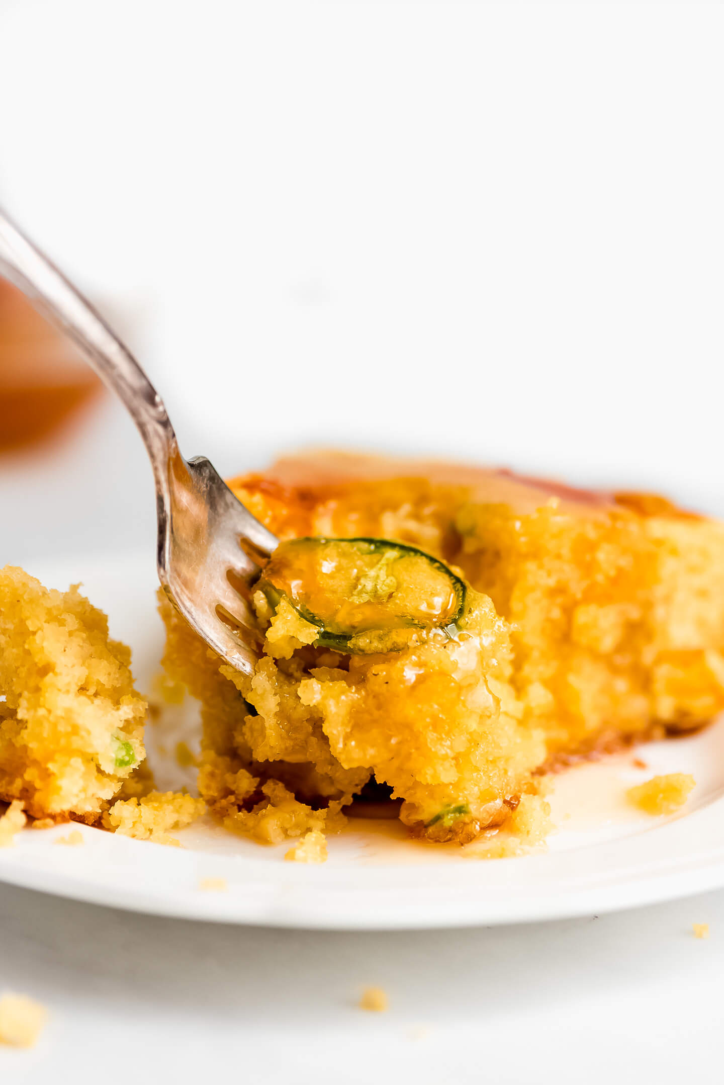 A fork lifting a bite of jalapeno cornbread drizzled with honey.