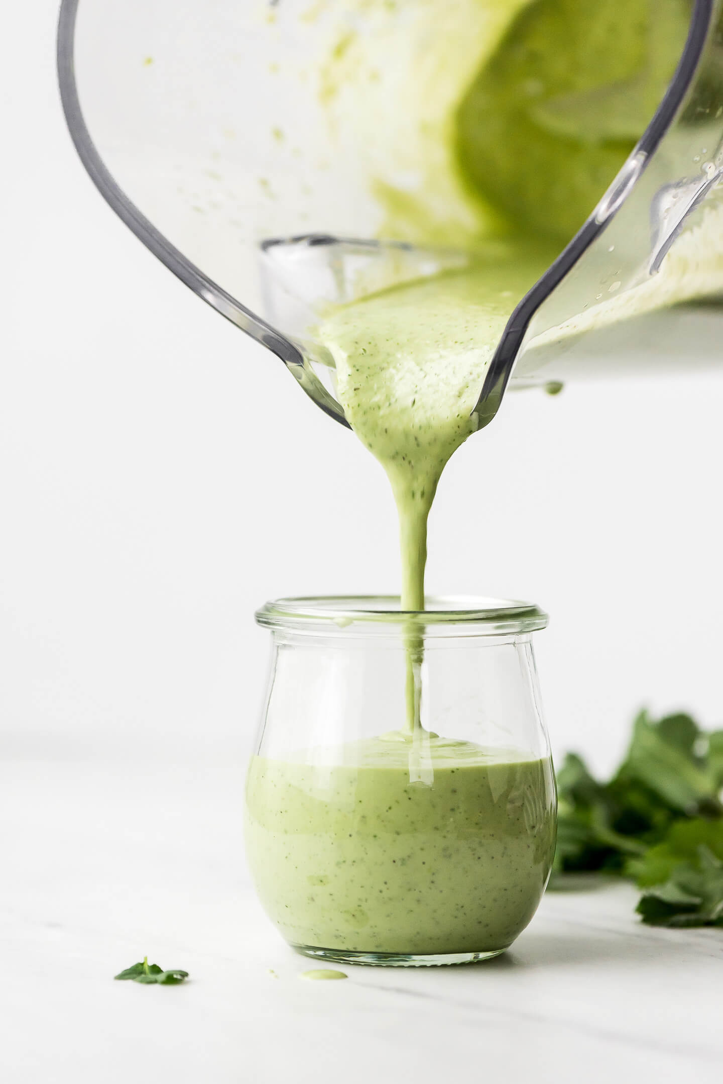 Green dressing being poured from a blender into a small Weck jar.