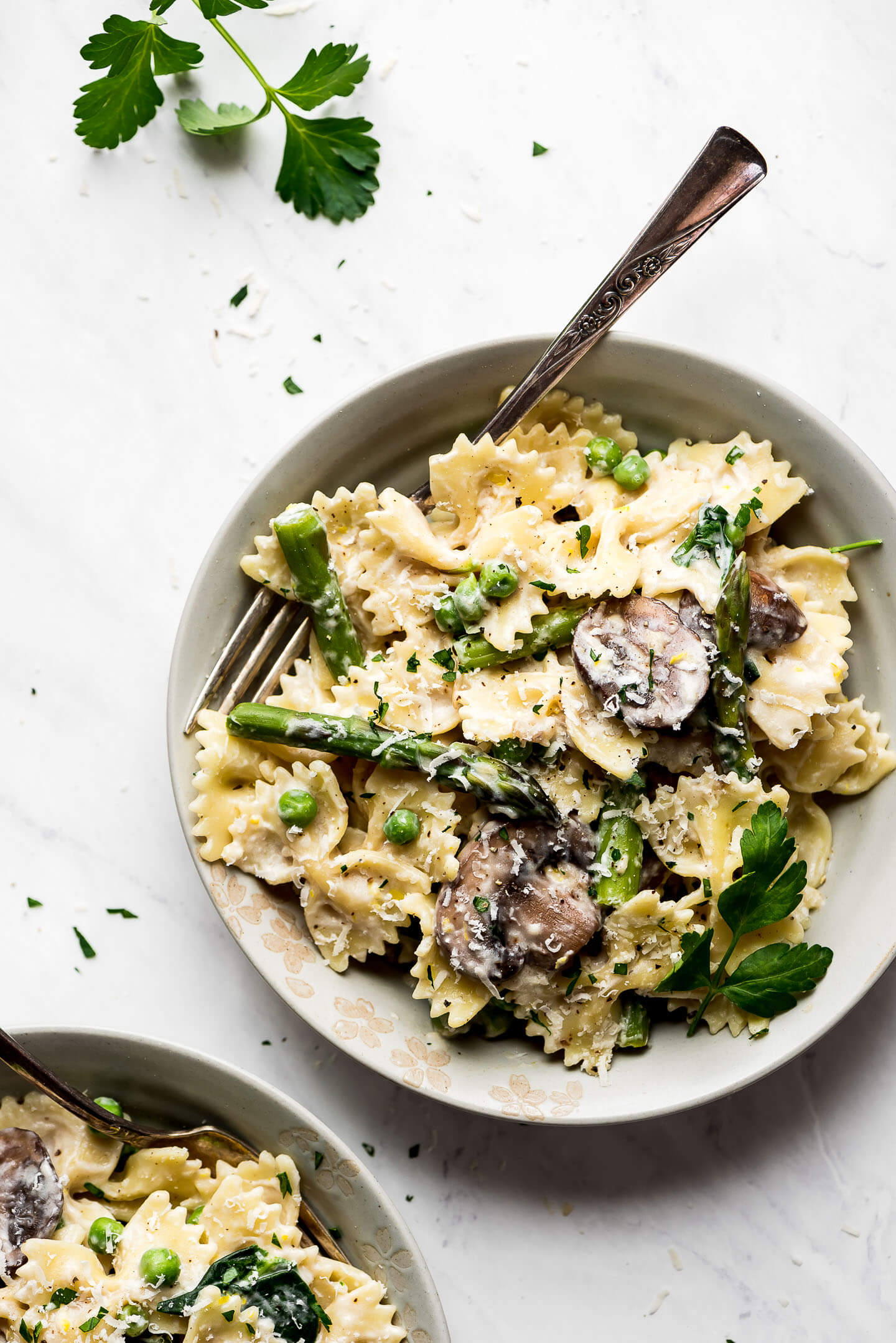 Two bowls of pasta with asparagus, mushrooms, peas and spinach.