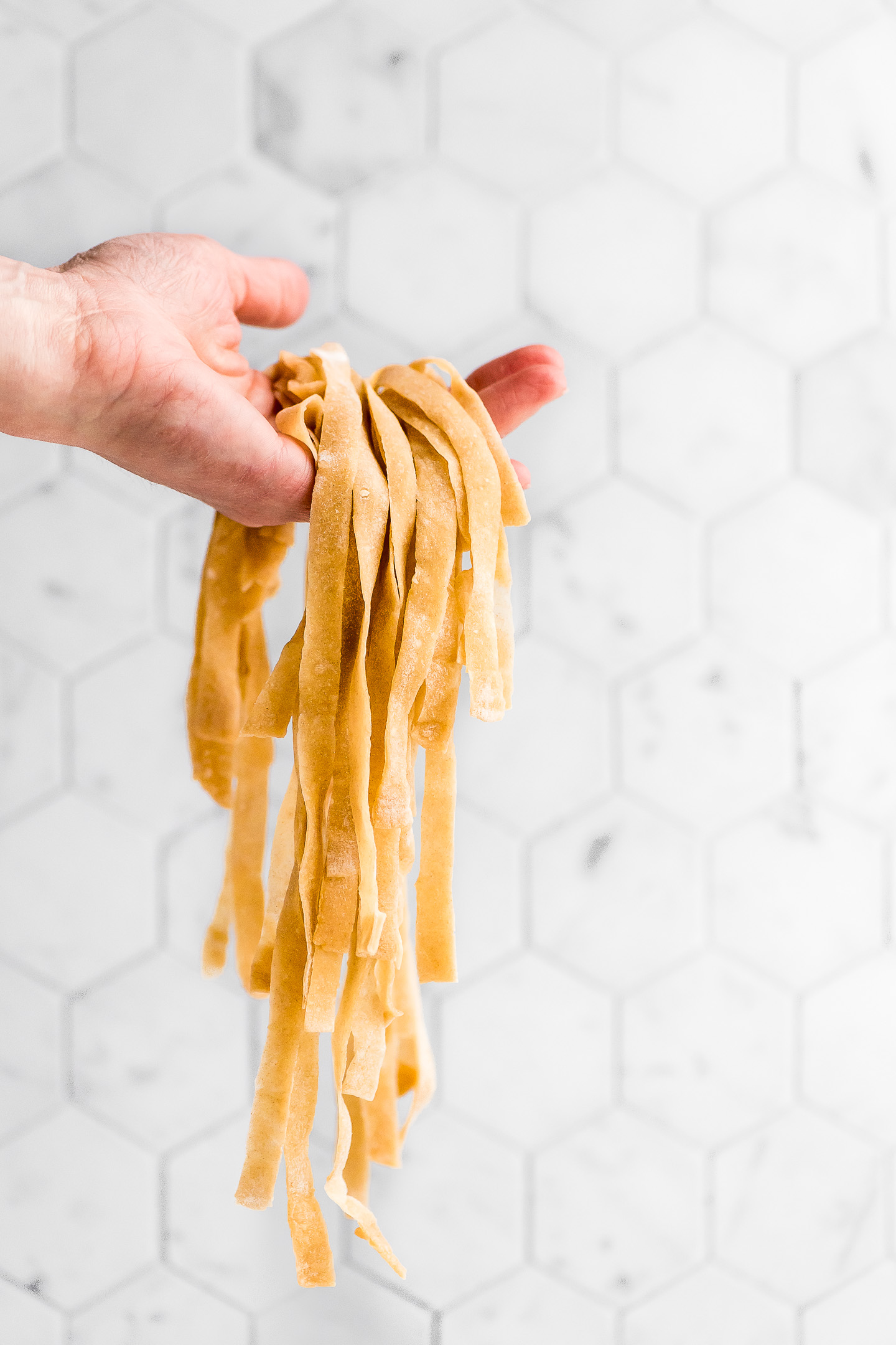 Fresh egg noodles draped over a hand and hanging down.