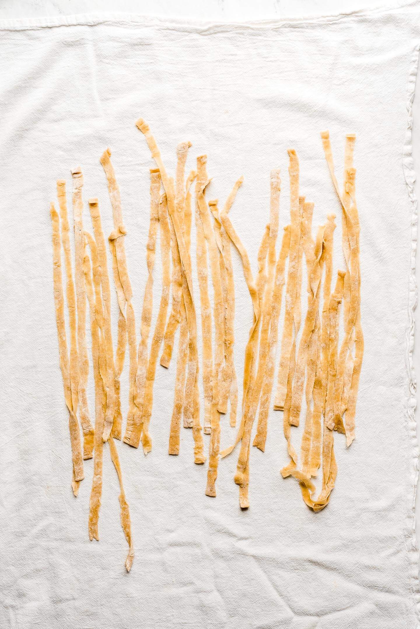 Long strands of egg noodles drying on a tea towel.