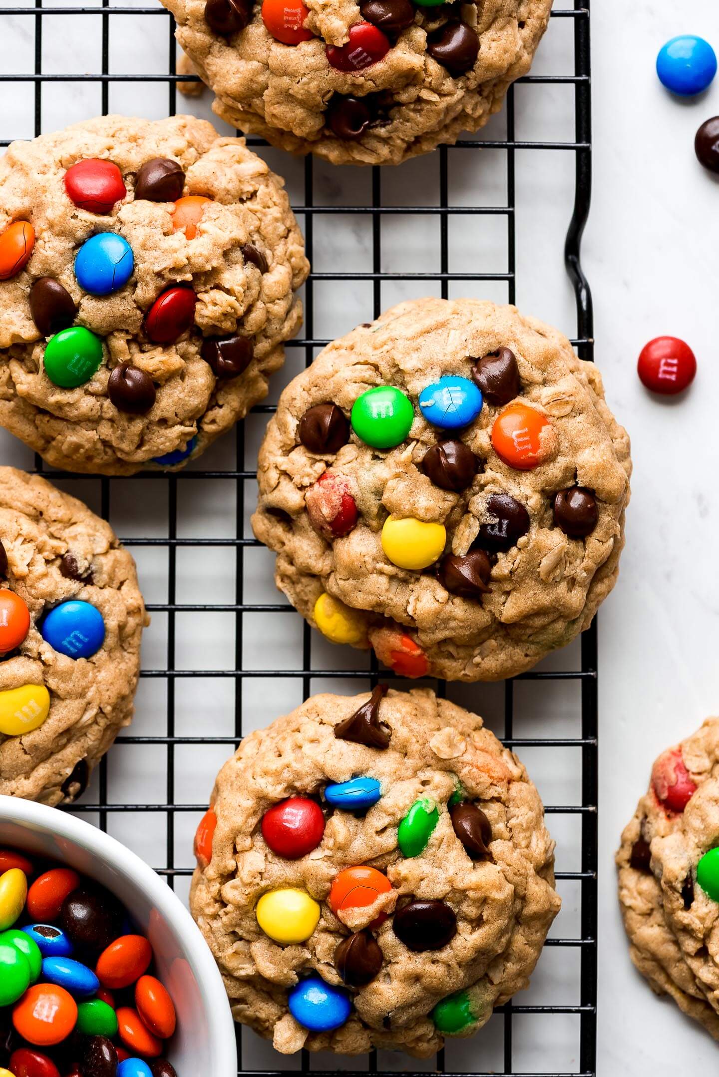 Monster Cookies on a cooling rack with a bowl of m&m's to the side.