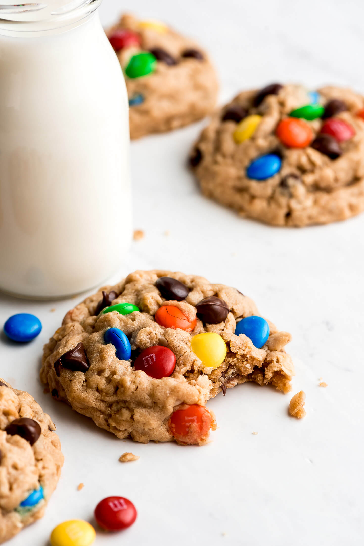 A Monster Cookie with M&M's and Chocolate Chips on top with a bite taken out and a glass of milk on the side.
