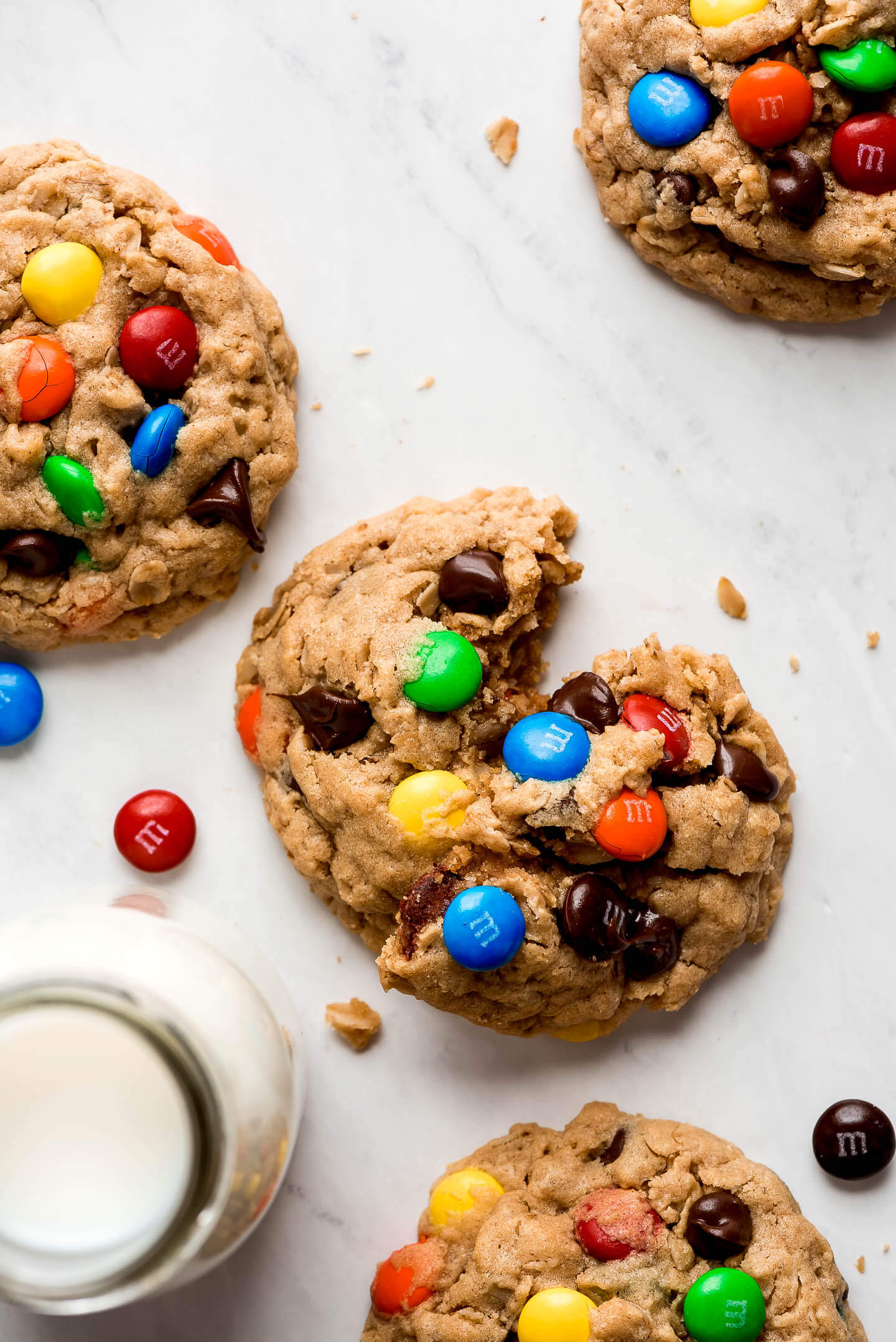 Peanut butter oatmeal cookies with chocolate chips and M&M's pressed into the top and a glass of milk to the side.