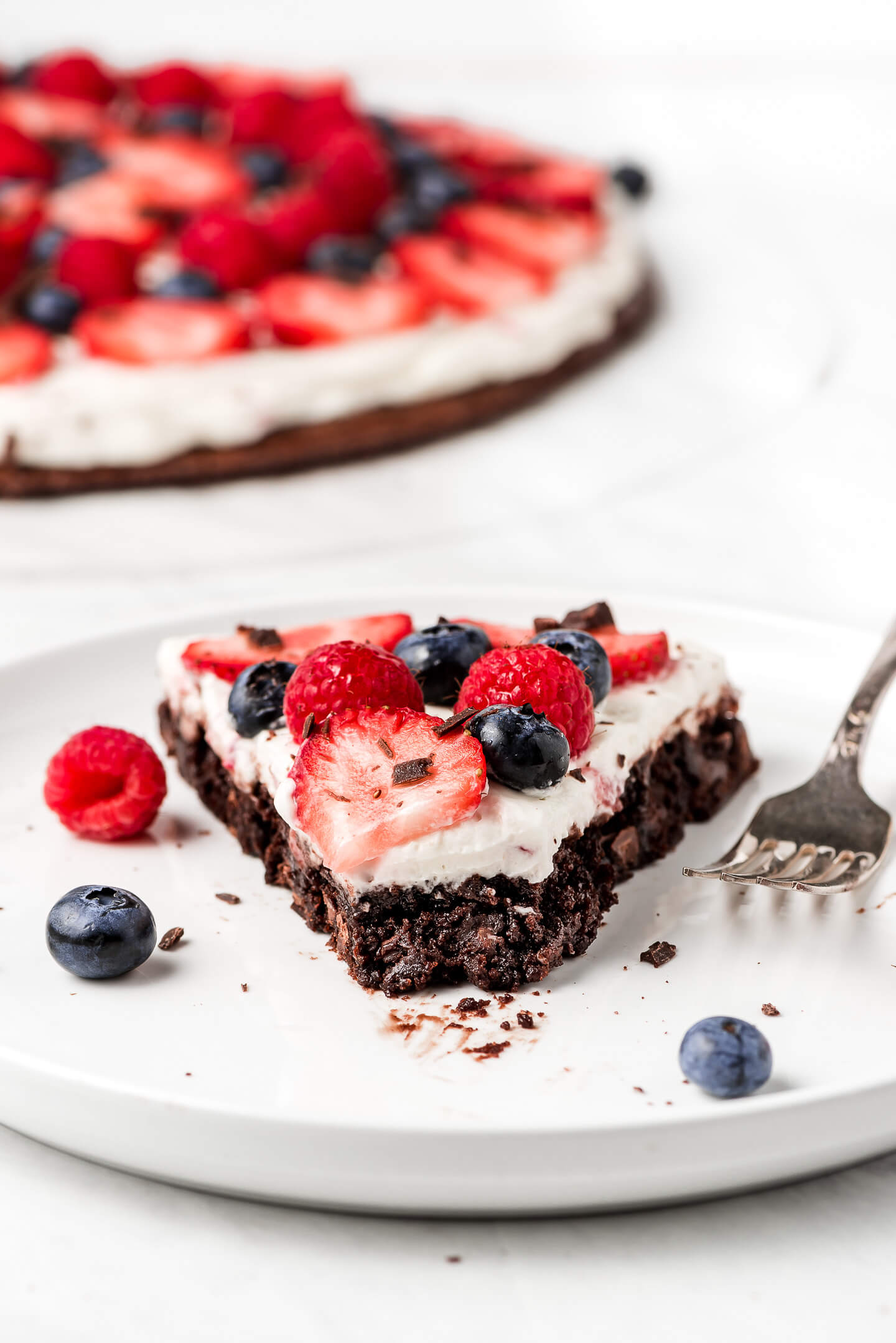 A slice of Brownie Pizza topped with a cheesecake spread and fresh berries.