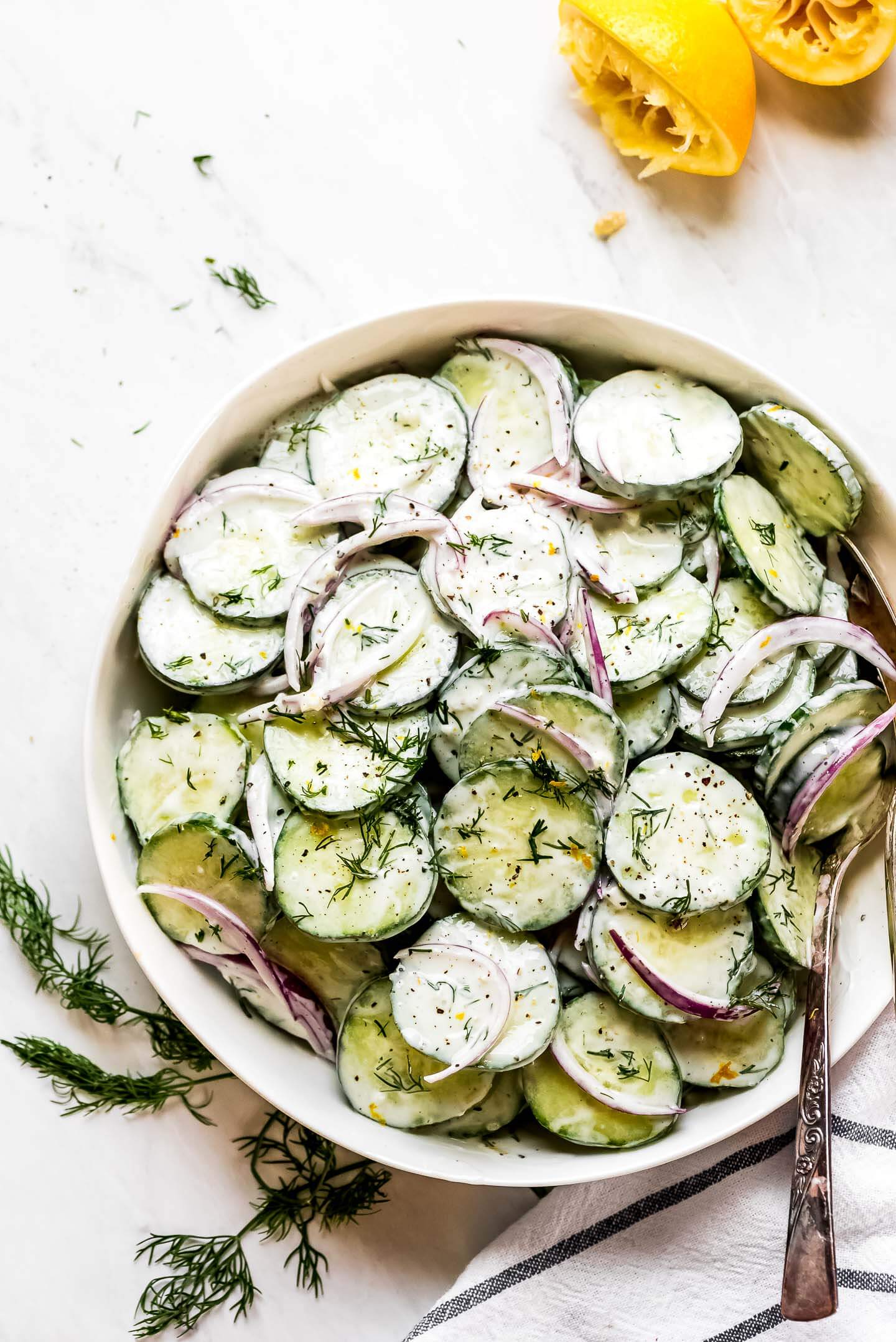 Sliced cucumbers and red onion slices in a bowl coated with a creamy sauce, fresh dill, lemon zest, and salt and pepper.