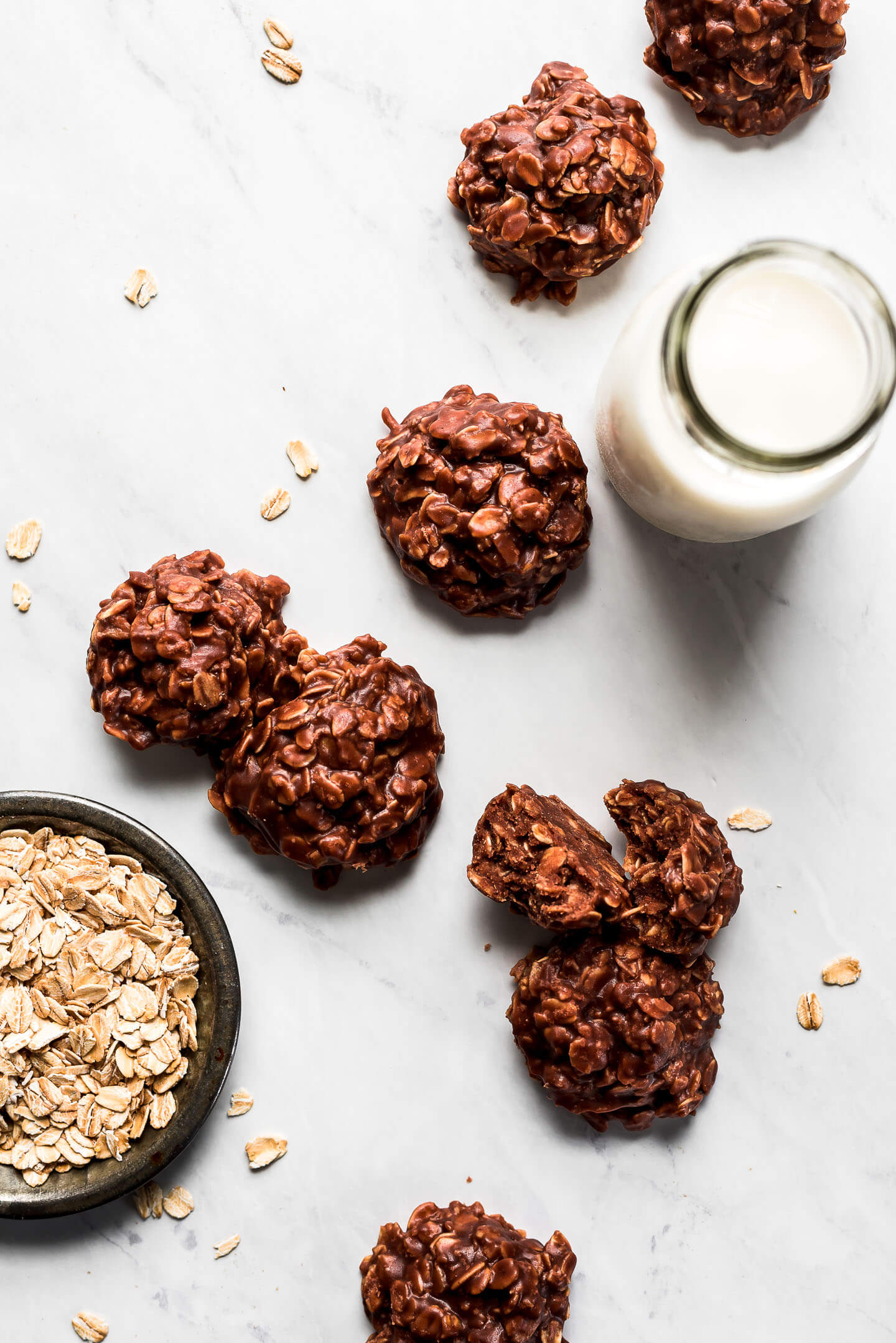 Chocolate Oatmeal Cookies on a marble surface with a jar of milk and small bowl of oats.