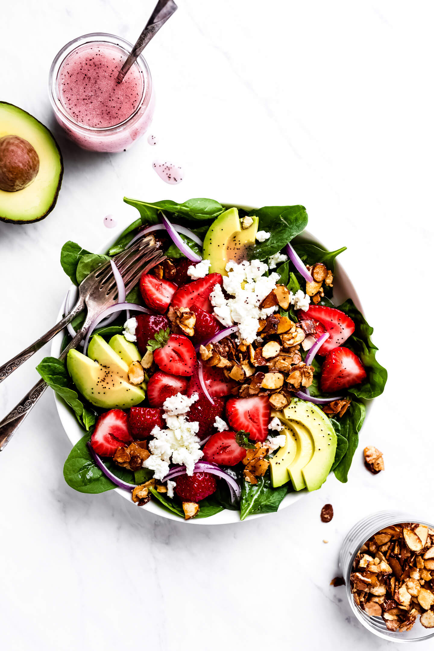 A strawberry and spinach salad with avocados and sliced almonds with poppy seed dressing.