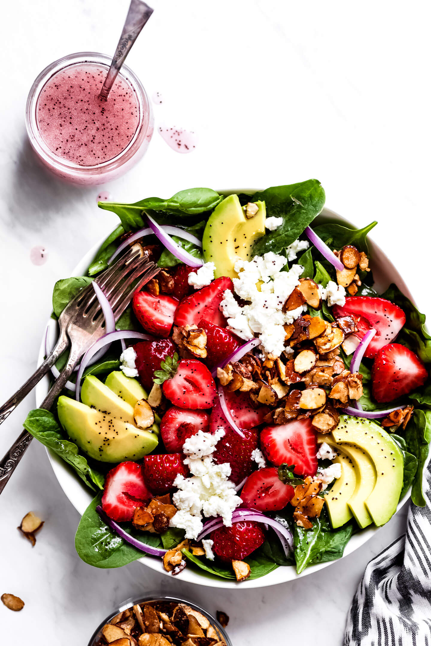 A Strawberry Spinach Salad topped with avocado, caramelized nuts, red onions, and goat cheese with poppy seed dressing on the side.