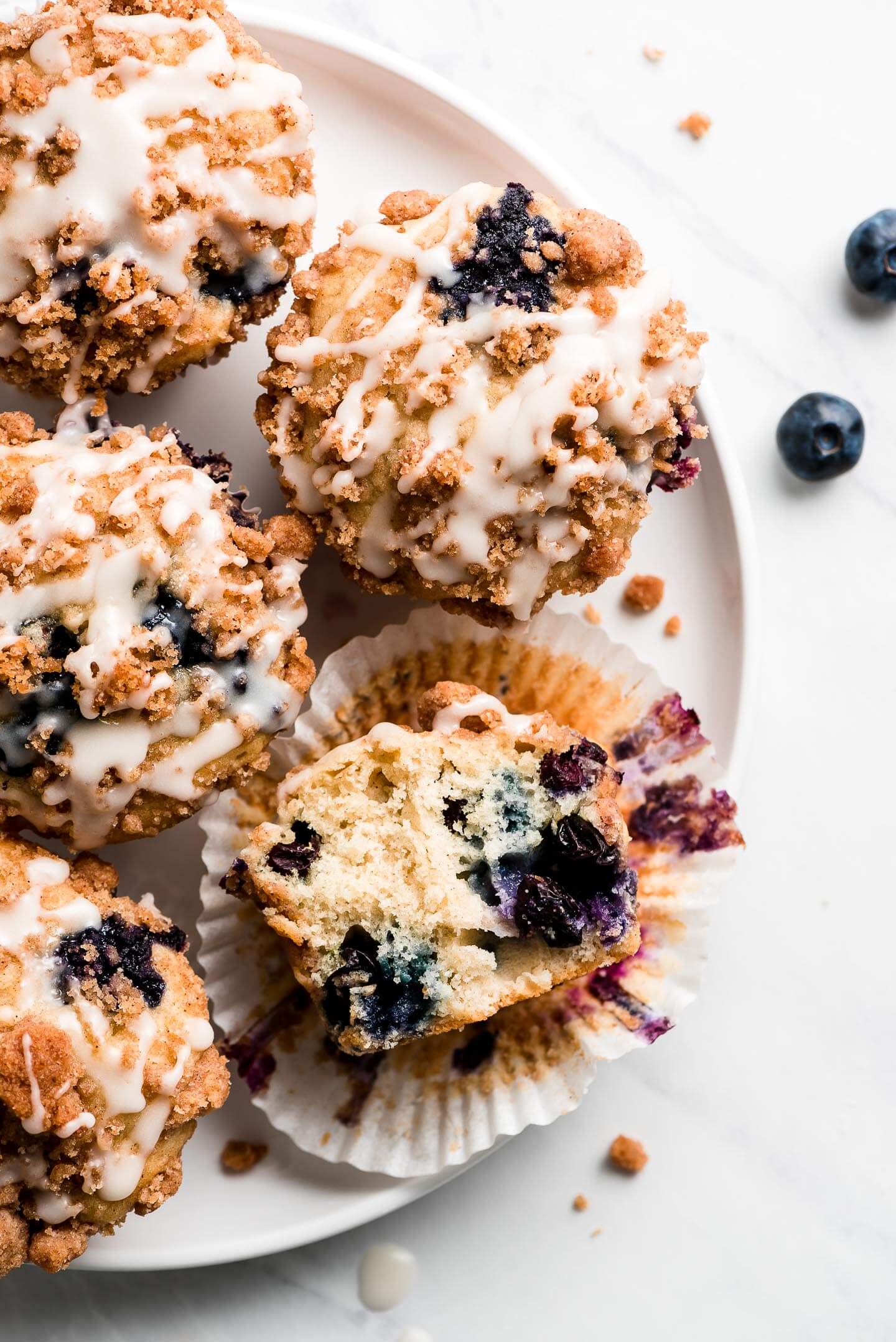 Streusel and icing topped blueberry muffins with one cut in half showing the fluffy tender crumb.