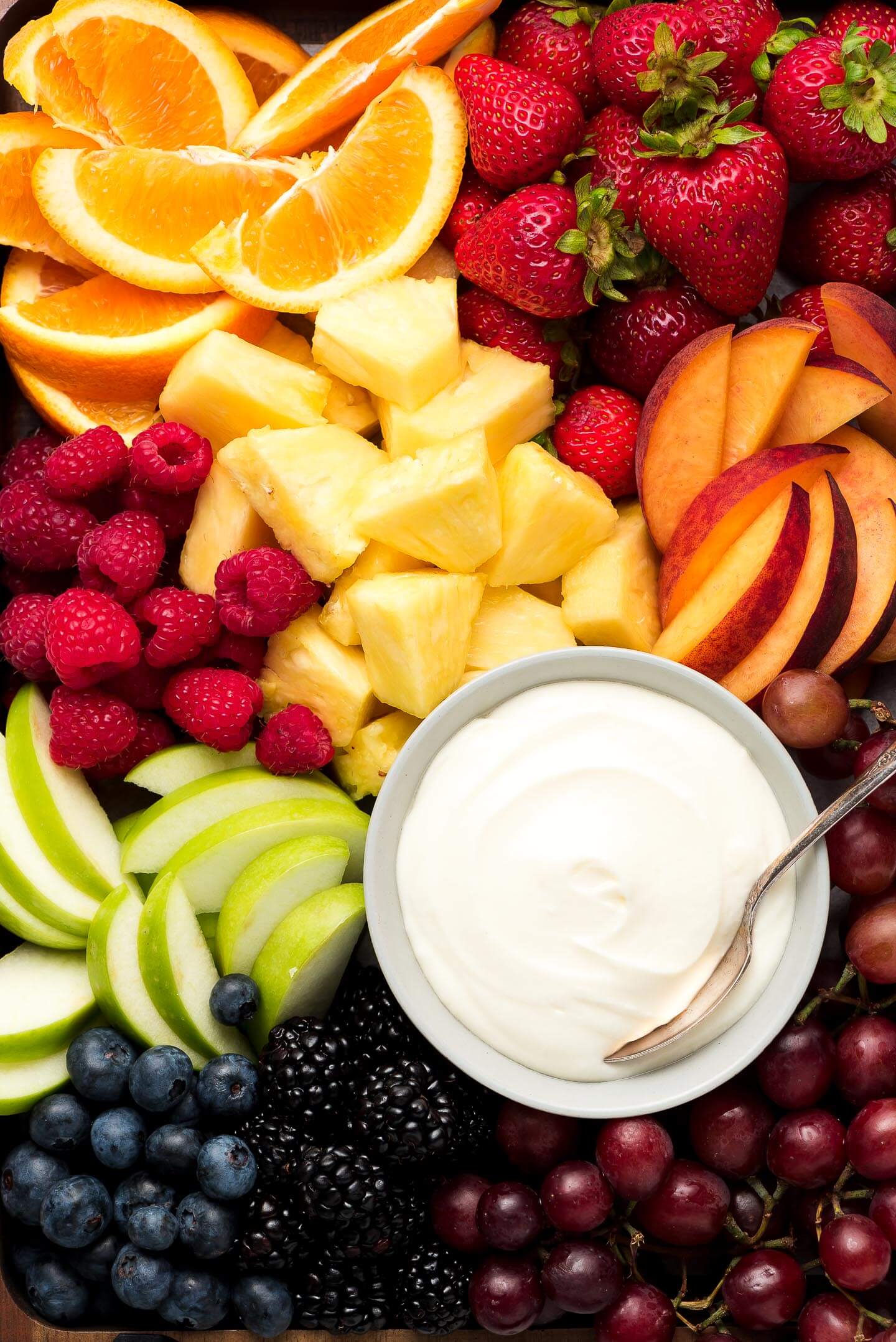 A close up of strawberries, oranges, raspberries, pineapple chunks, peaches slices, apple slices, blueberries, blackberries, red grapes, and fruit dip.