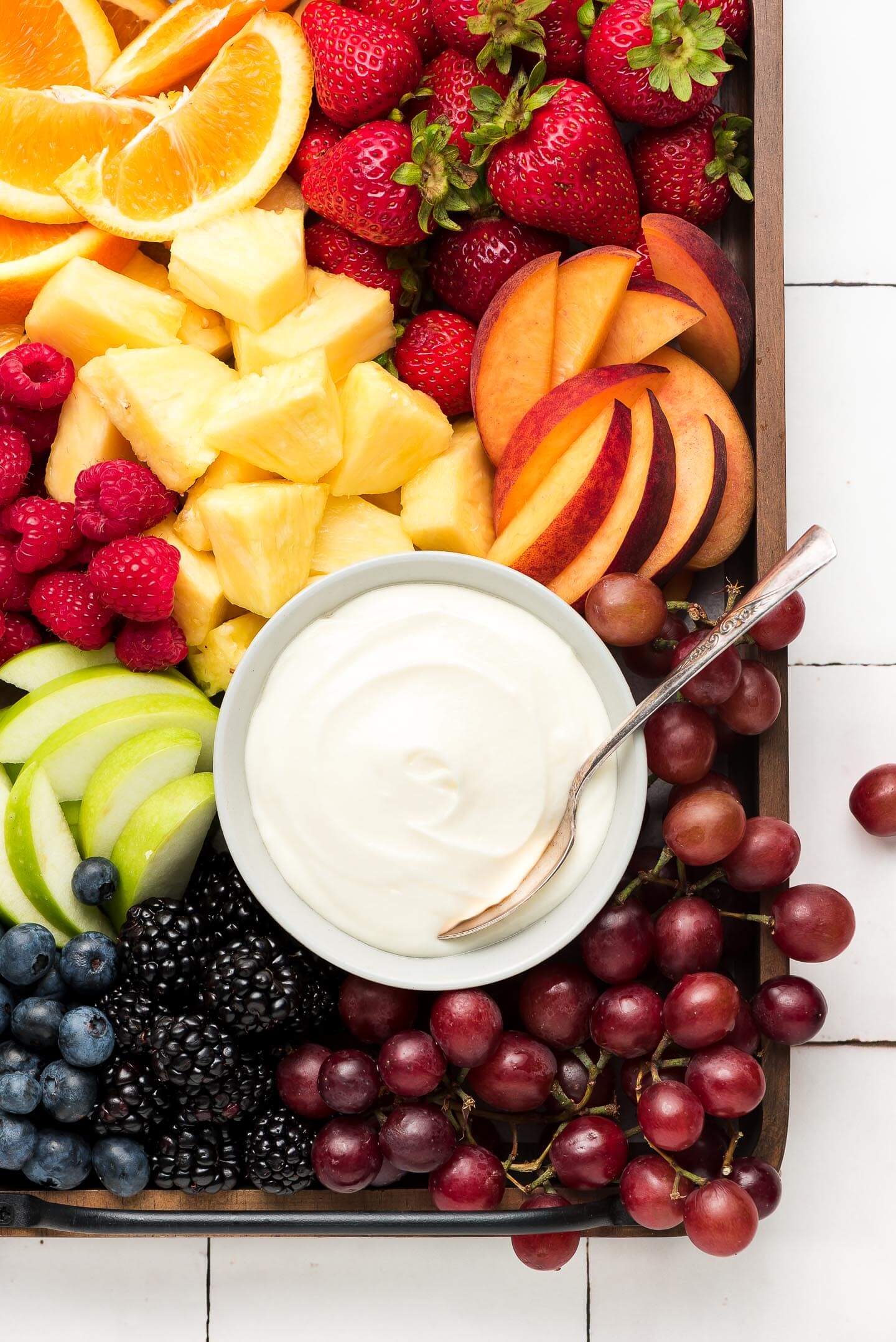 A wooden tray of fruit and Cream Cheese Fruit Dip on a tile surface.