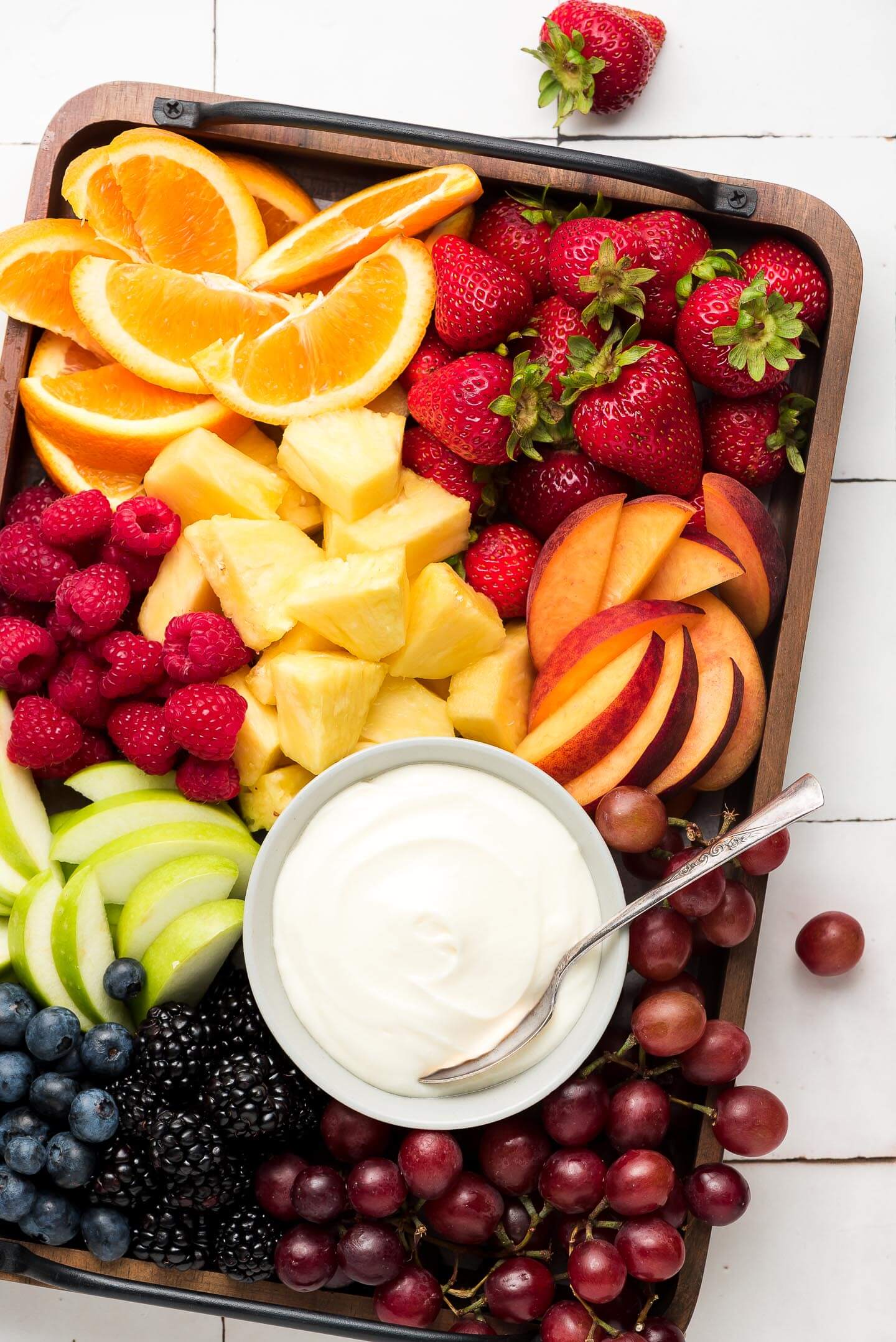 A big wooden tray loaded with colorful fruit and a small bowl of marshmallow fruit dip.