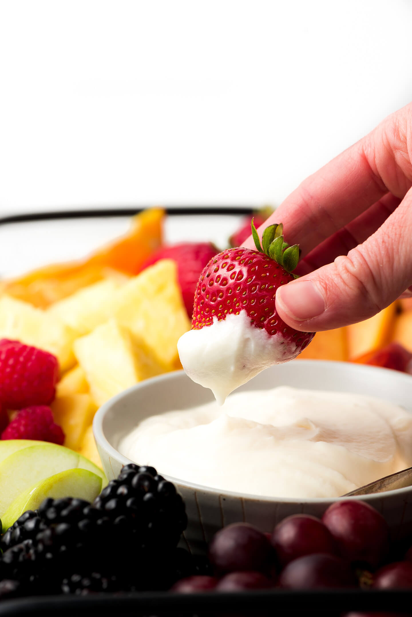 Dipping a strawberry into a white creamy dip.