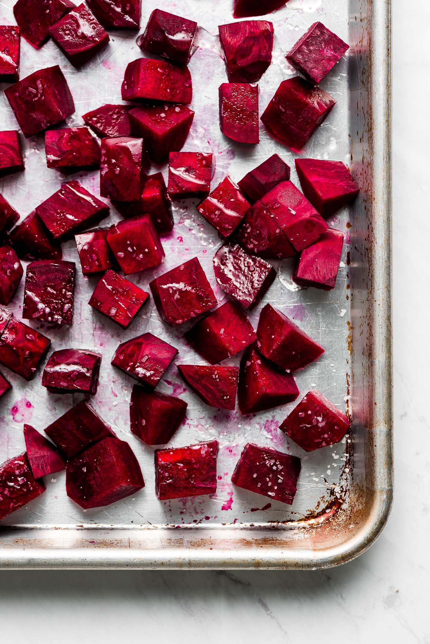 A baking sheet with raw diced beets drizzled with olive oil and sprinkled with kosher salt.