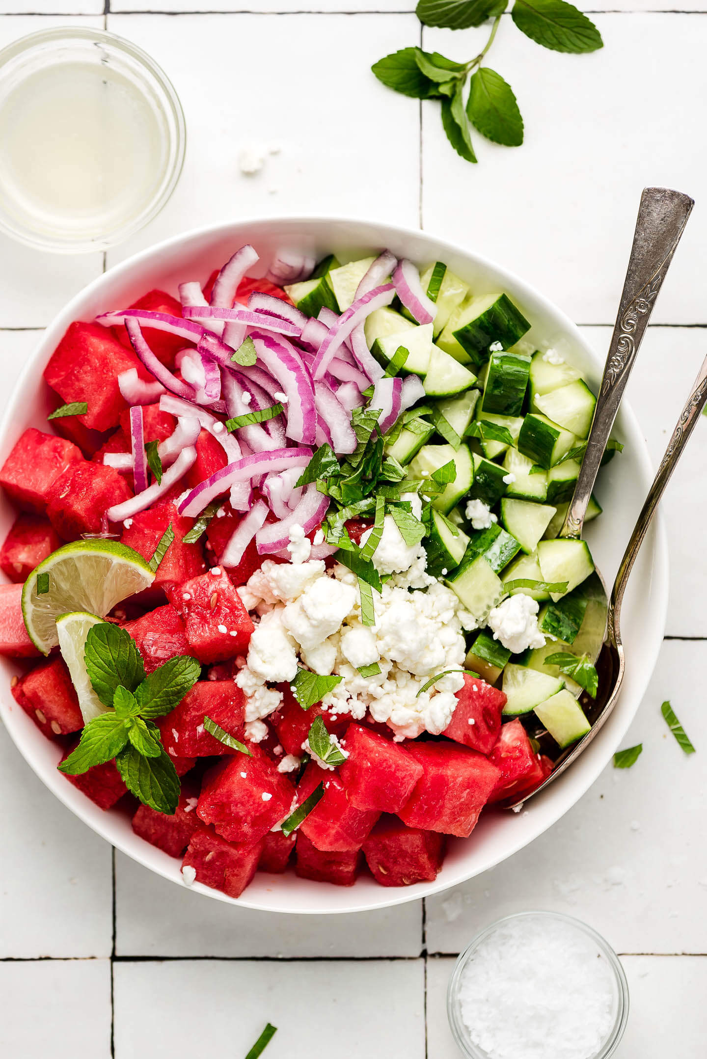 Watermelon, red onion, chopped cucumber, feta cheese, lime slices, and chopped mint in a bowl.