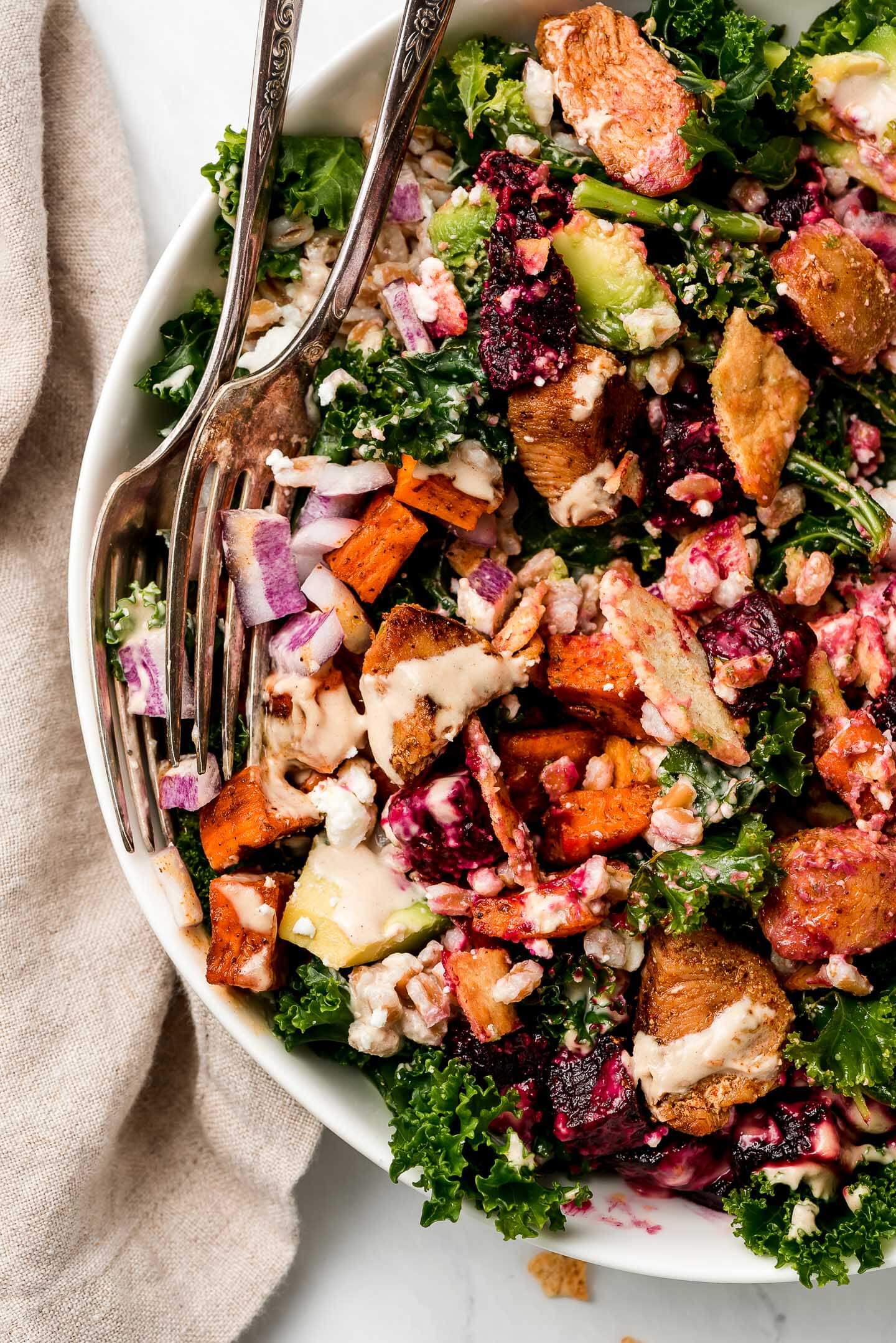 Kale Salad with roasted vegetables and drizzled with tahini dressing with two forks in the side.