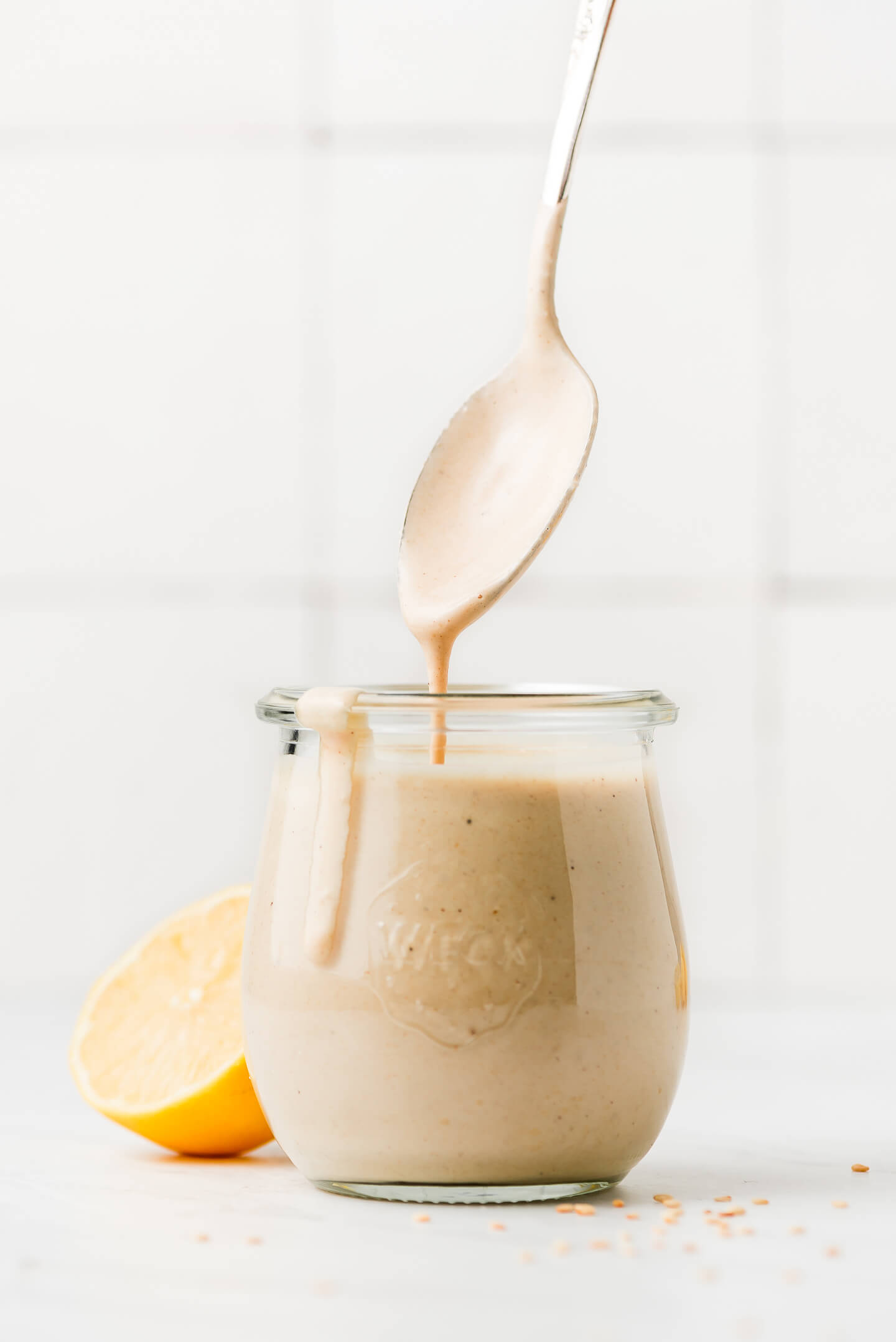 A straight on shot of a  jar of Lemon Tahini Dressing with a spoon lifted straight up out of the jar.
