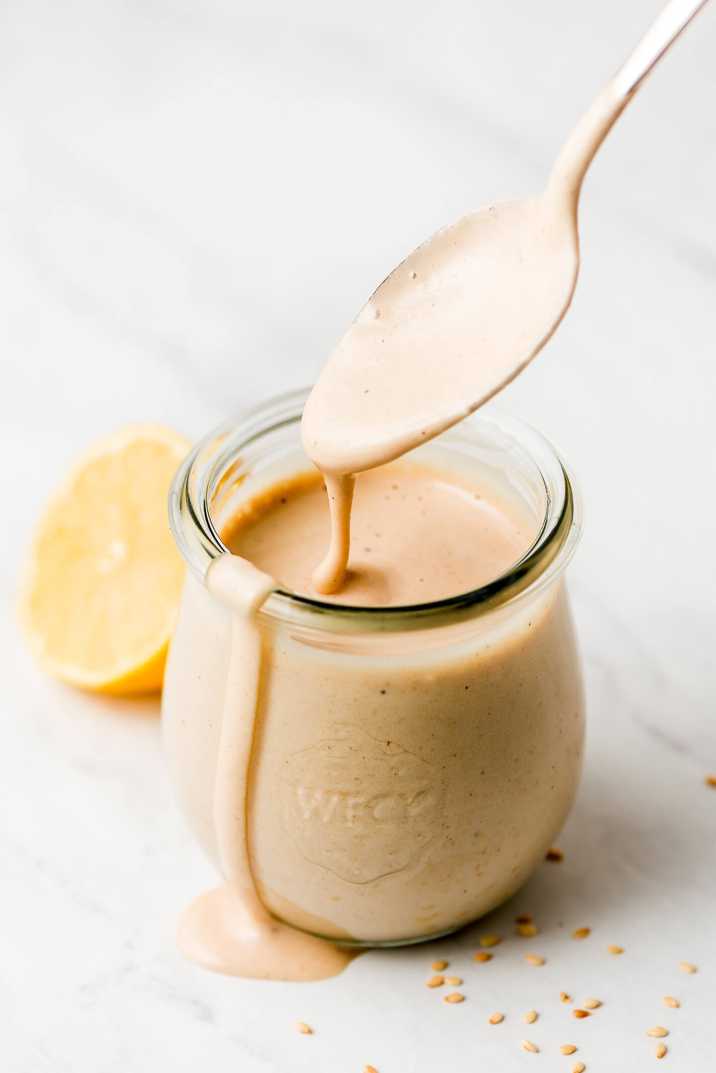 A jar of Lemon Tahini Dressing with a spoon lifting some out and letting it drizzle back into the jar.