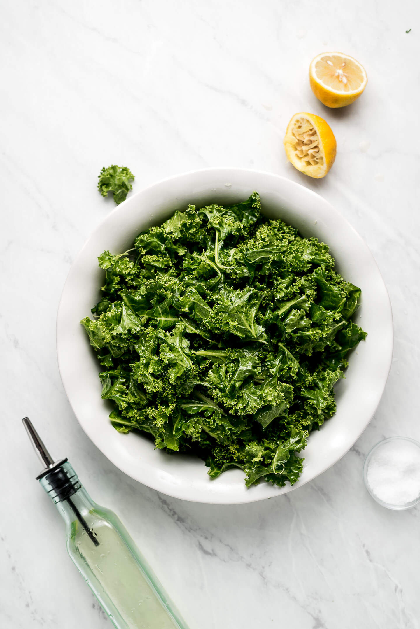 Massaged Kale in a shallow bowl with a squeeze lemon, bottle of oil, and bowl of salt to the sides.