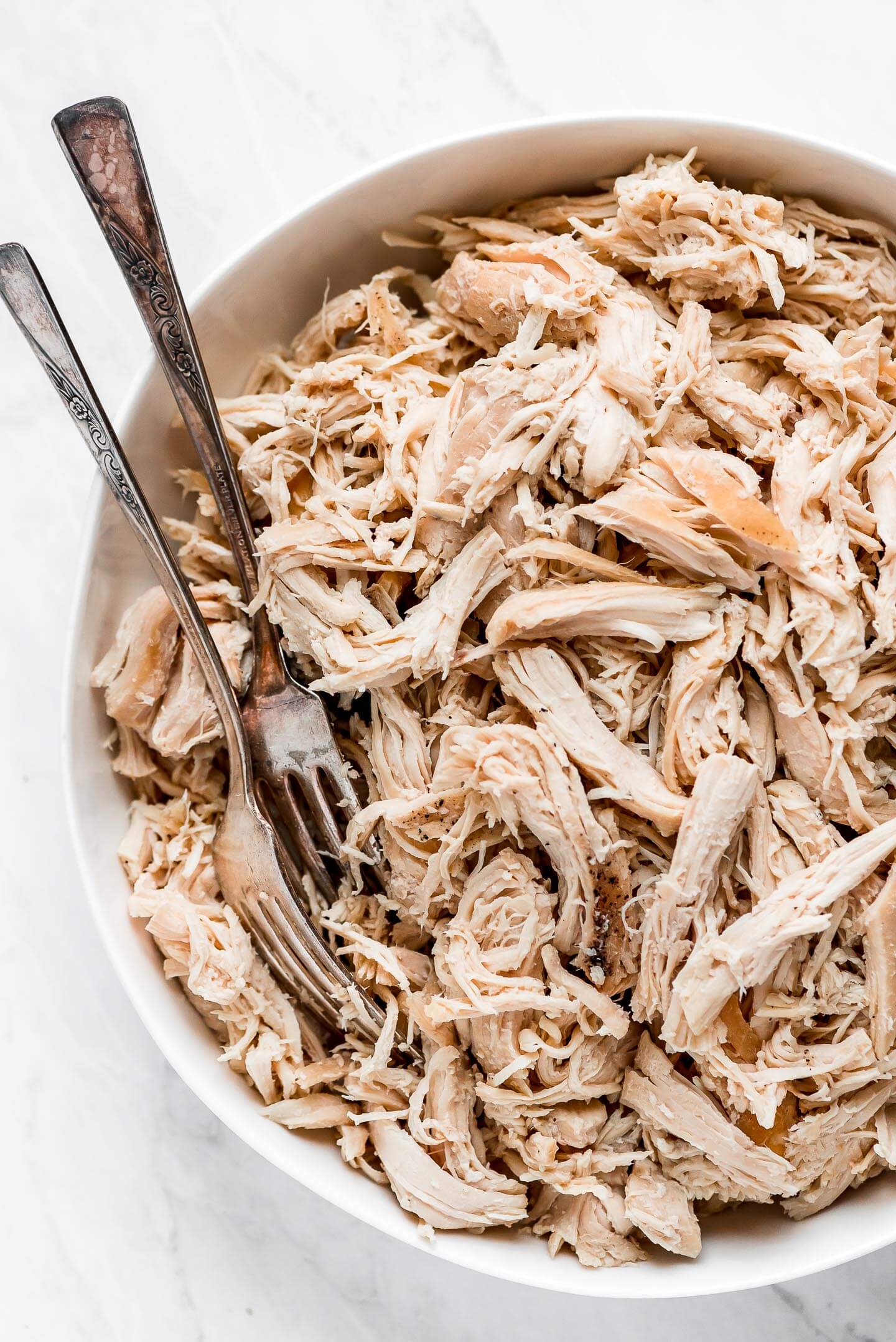 Top view of shredded chicken in a bowl with two forks in the side of the bowl.