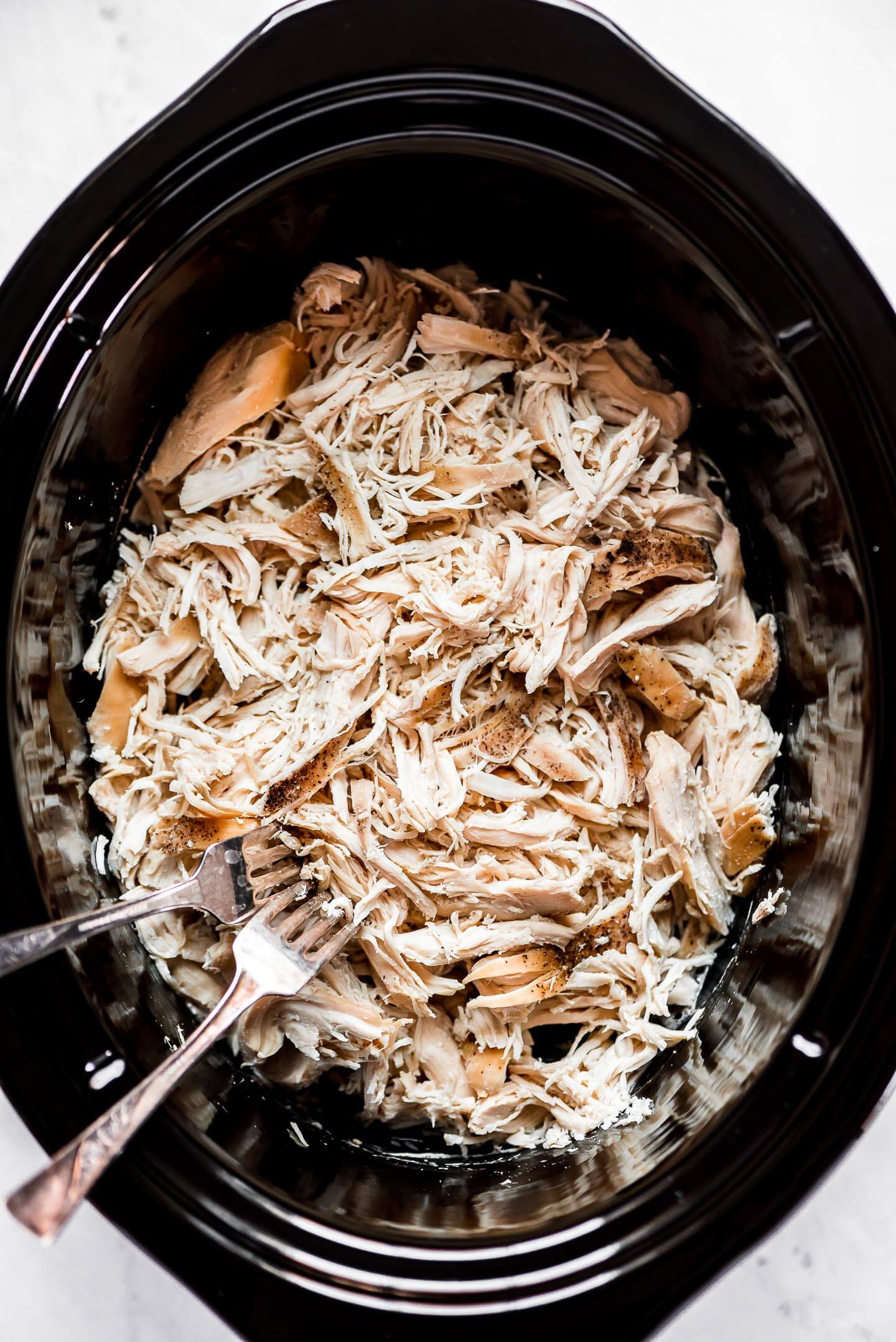 Top view of shredded chicken in a slow cooker with two forks at the side that were used for shredding.
