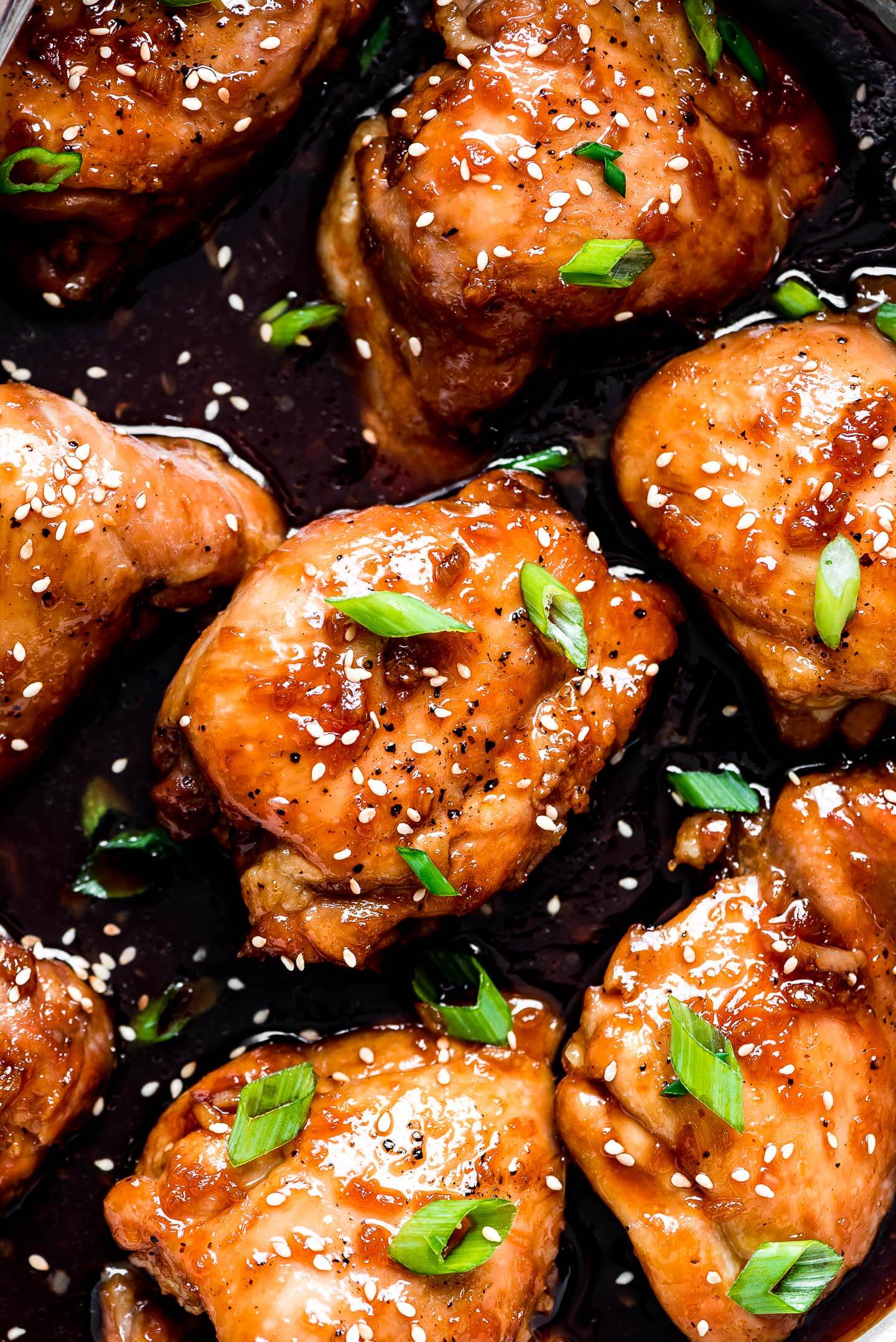 A close-up shot of glazed chicken thighs garnished with toasted sesame seeds, and green onions.