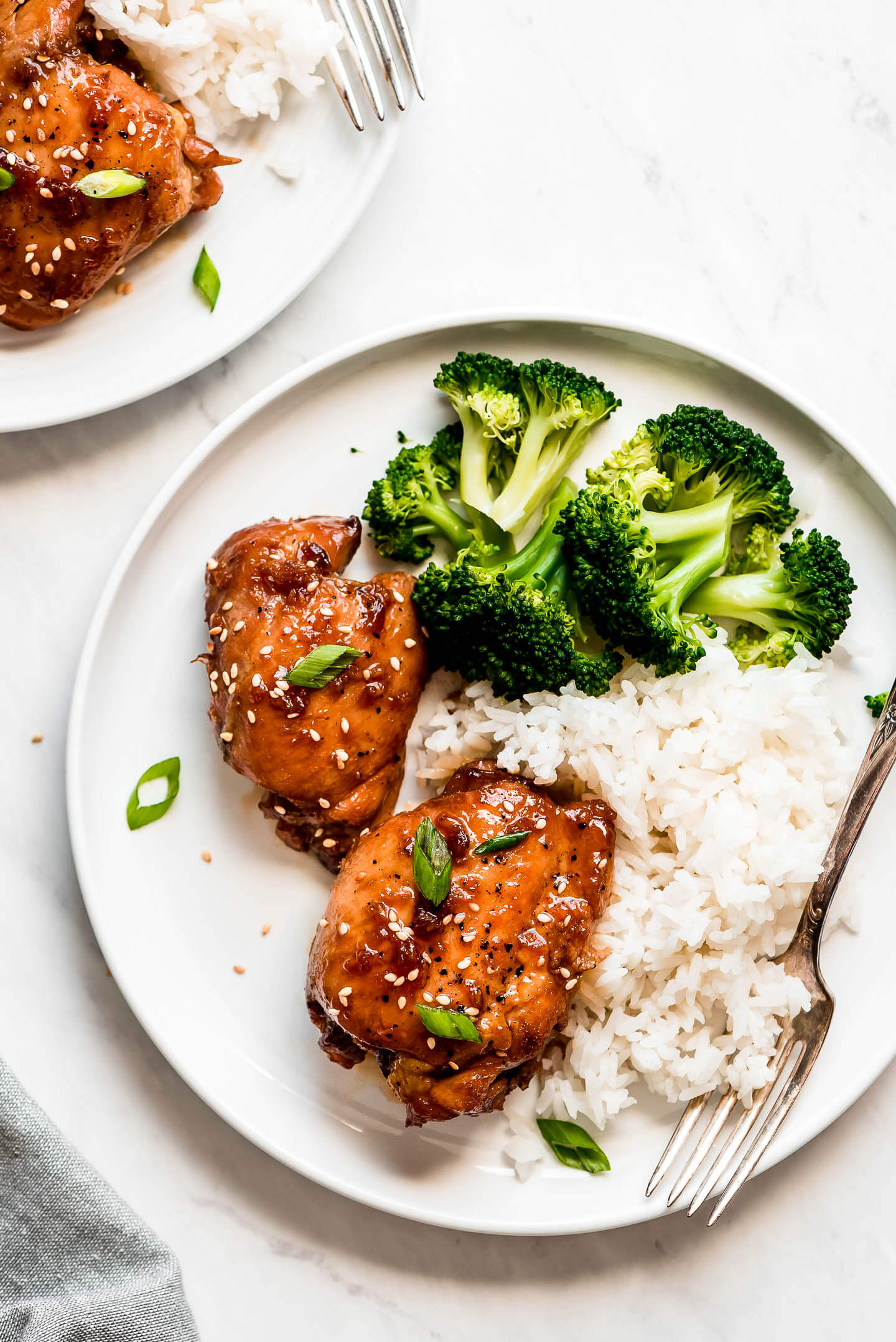 Plates of glazed chicken thighs, white rice, and broccoli.