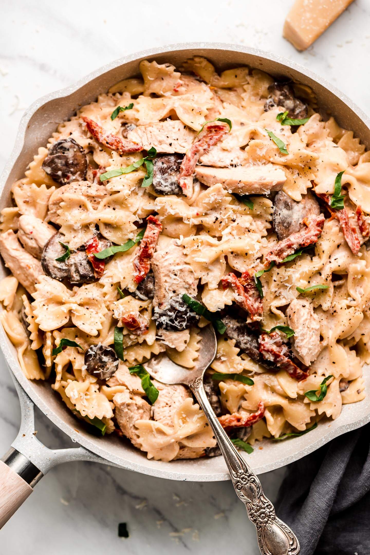 A pan of creamy bow tie pasta with mushrooms, chicken, sun dried tomatoes, basil, and Parmesan cheese.