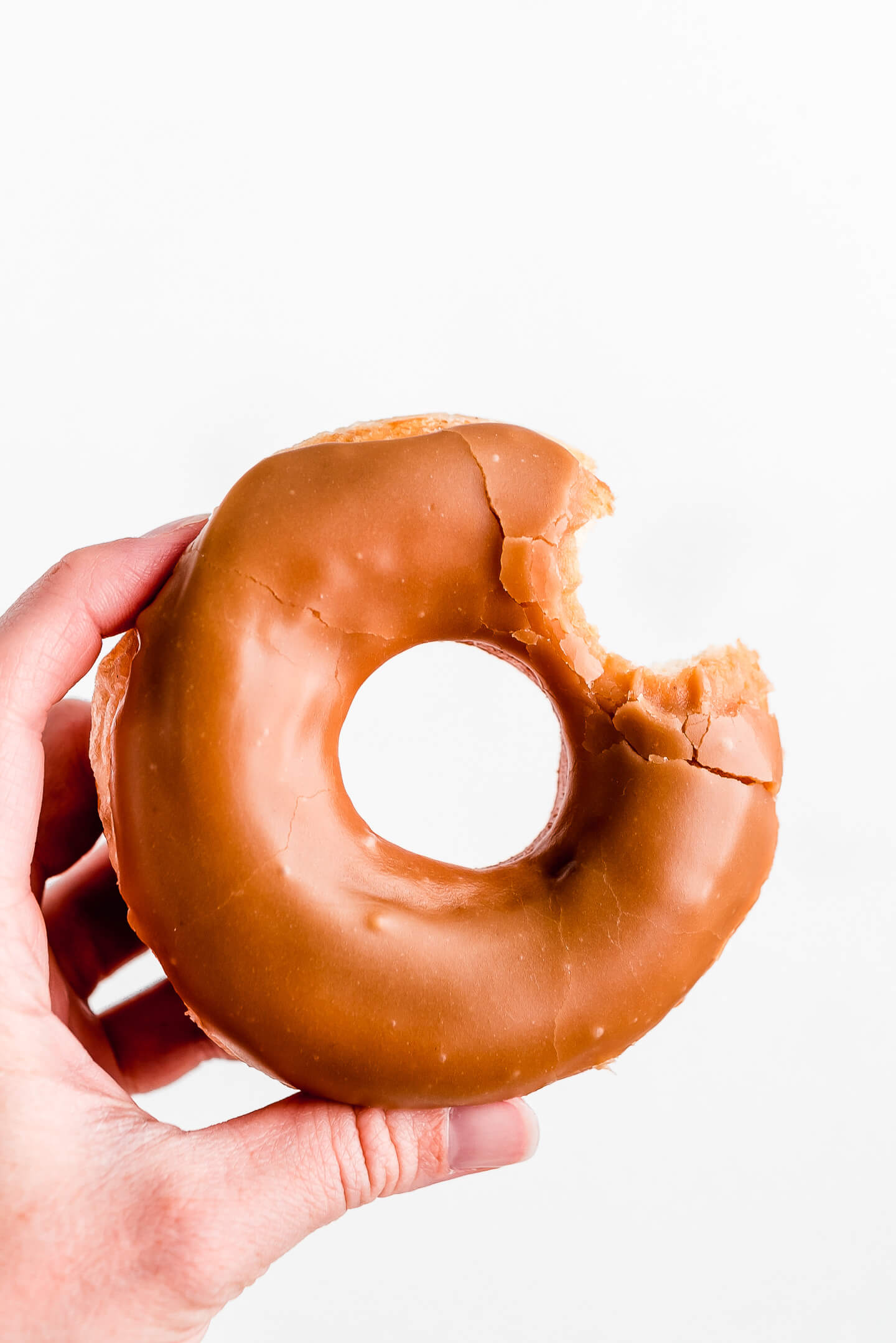 A hand holding up a Maple Donut with a bite taken out.