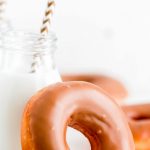 A maple glazed donut leaning against a jar of milk with a straw in it.