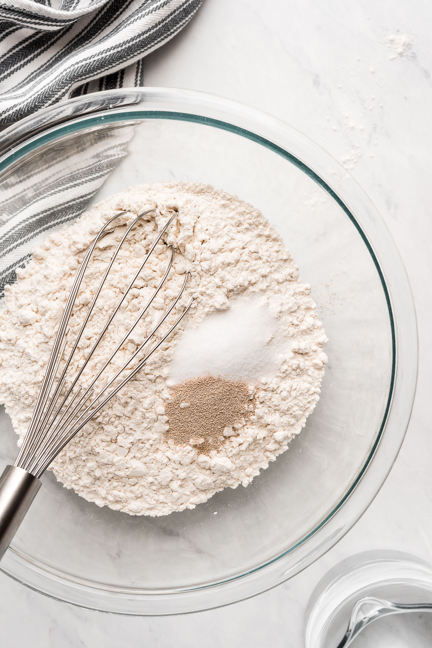 A glass mixing bowl with flour, salt, and yeast.