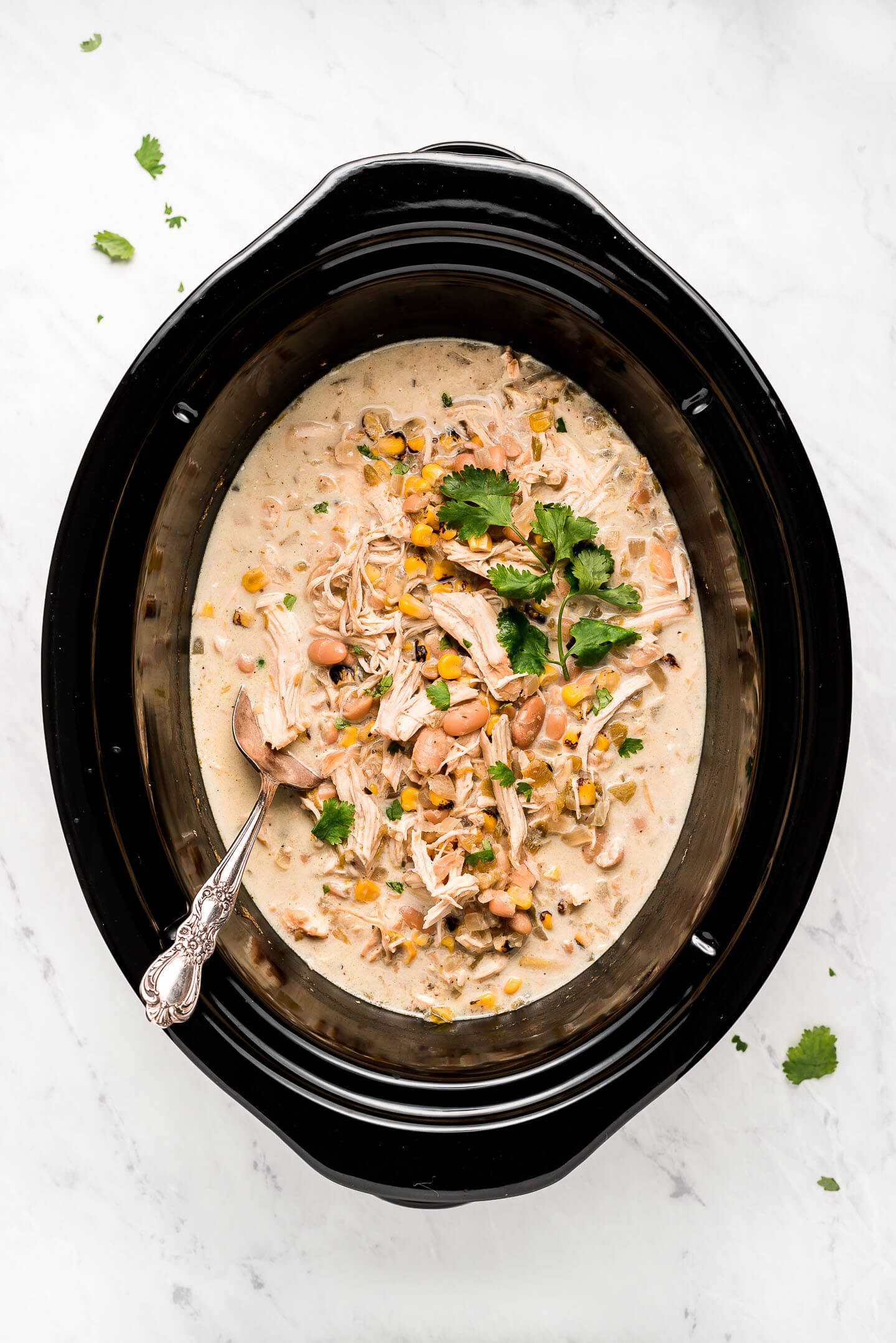 A slow cooker filled with a white creamy soup with chicken corn, white beans, and cilantro.