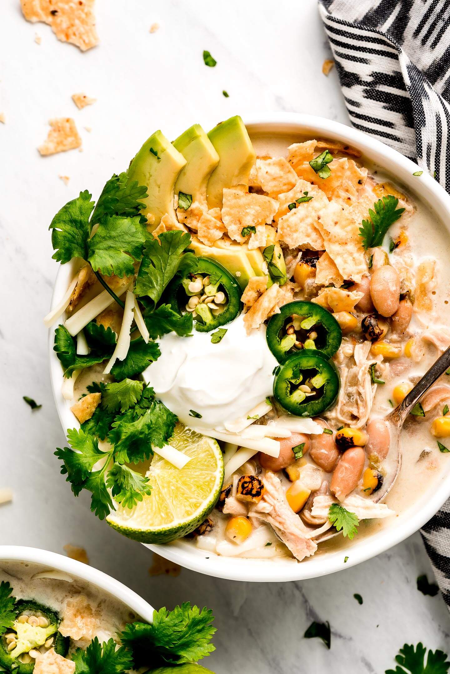 White Chicken Chili in a bowl topped with avocado slices, cilantro, jalapeno, chips, cheese, sour cream, and a lime.